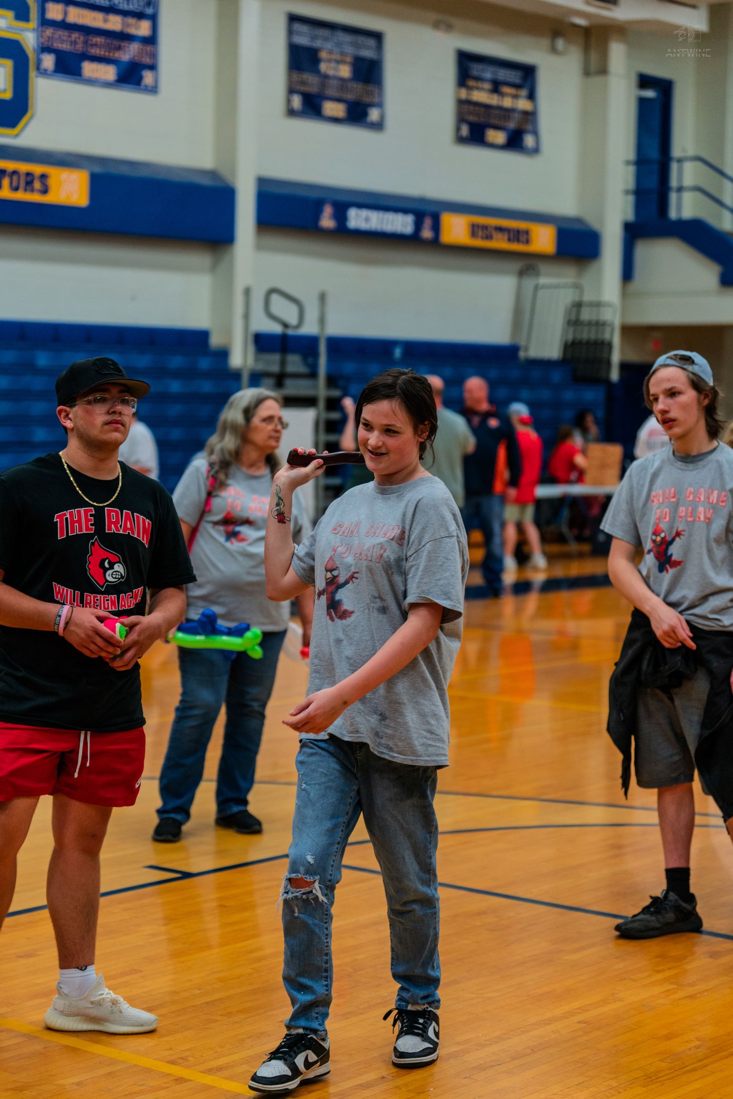 Students in matching red and gray team shirts stand on a school gymnasium floor during an indoor sporting event.