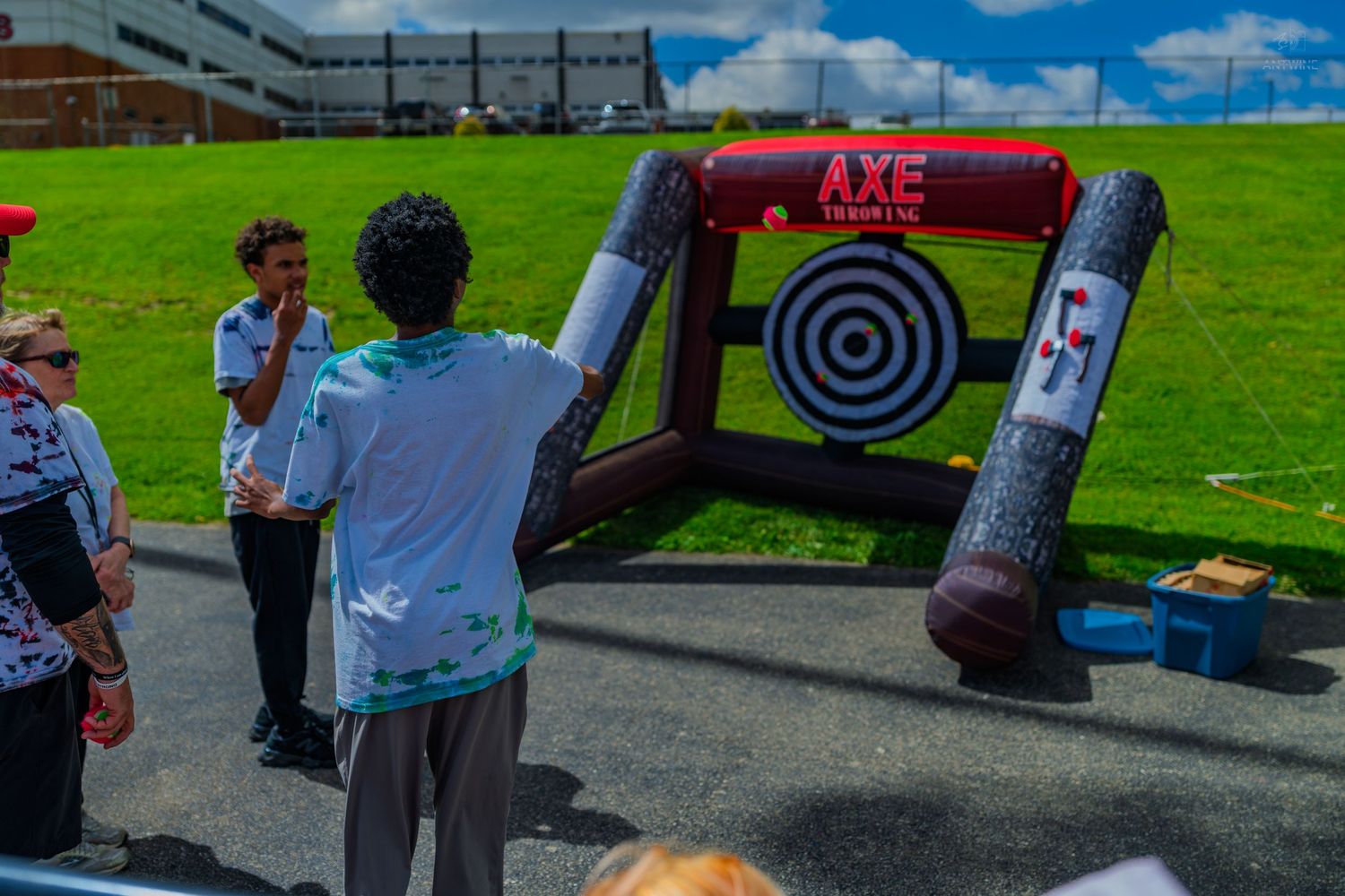 People playing inflatable axe throwing game on green grass at outdoor event on sunny day.