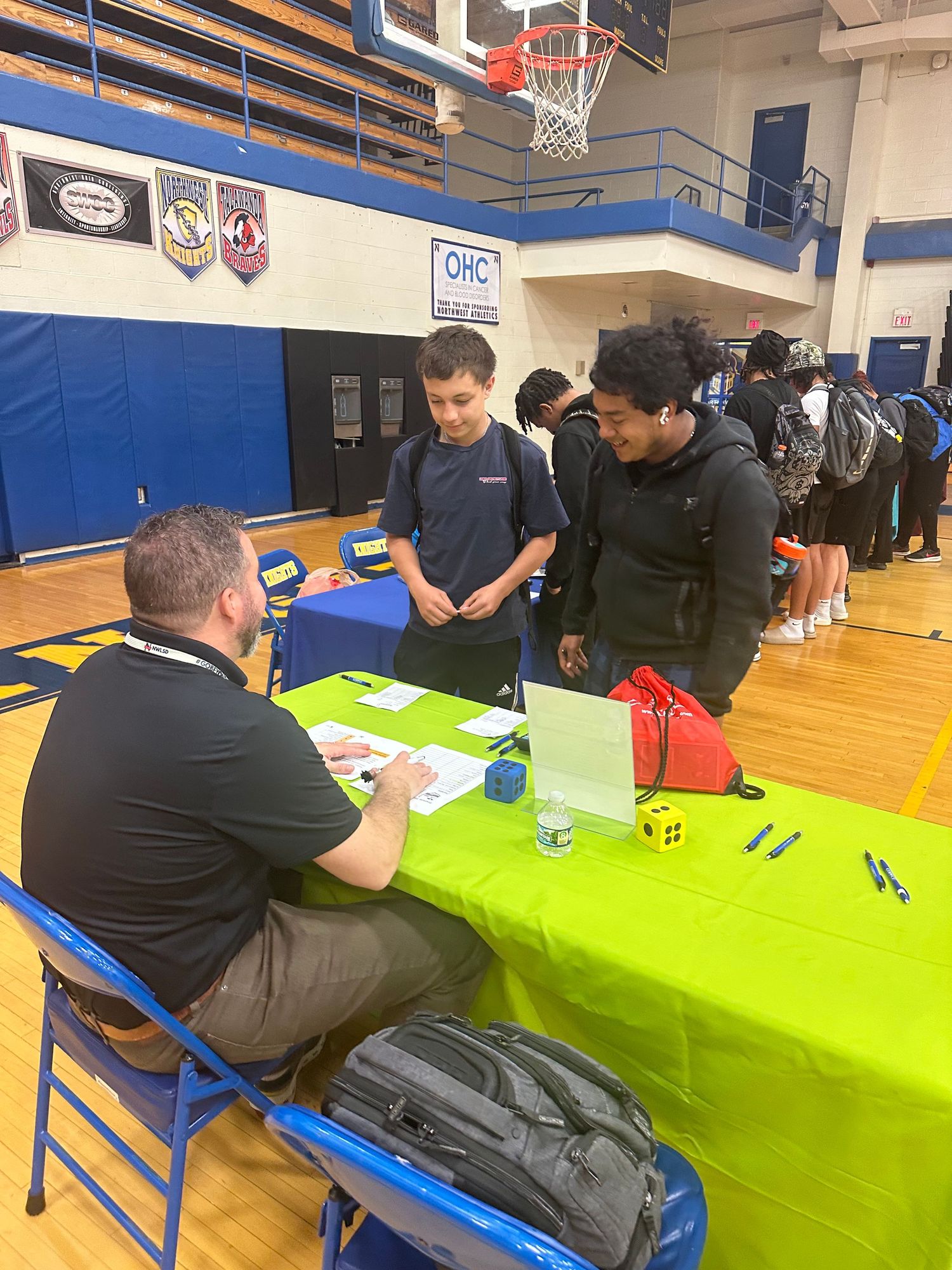 Students speak with a recruiter at a lime green table during a school career fair in a gymnasium.