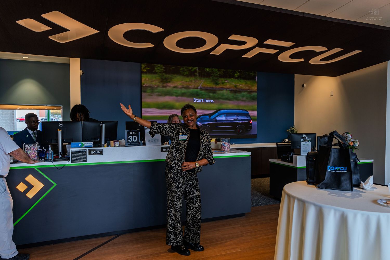 COPFCU credit union branch interior with staff member presenting services at modern teller counter during grand opening.
