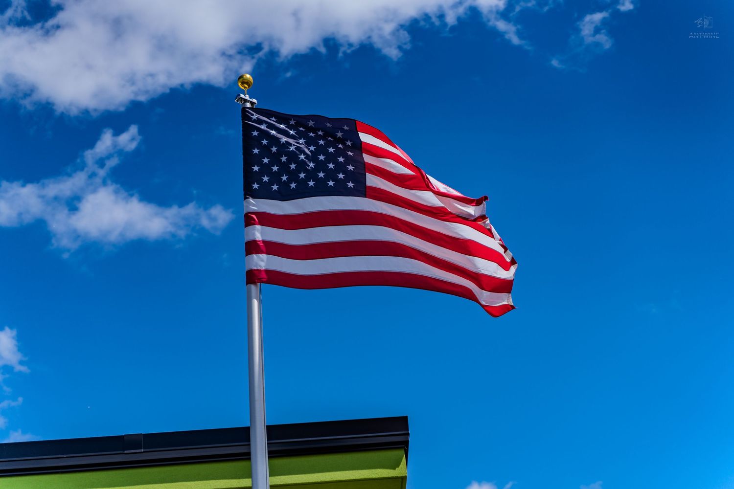 American flag waving proudly on a flagpole against a bright blue sky with white clouds.