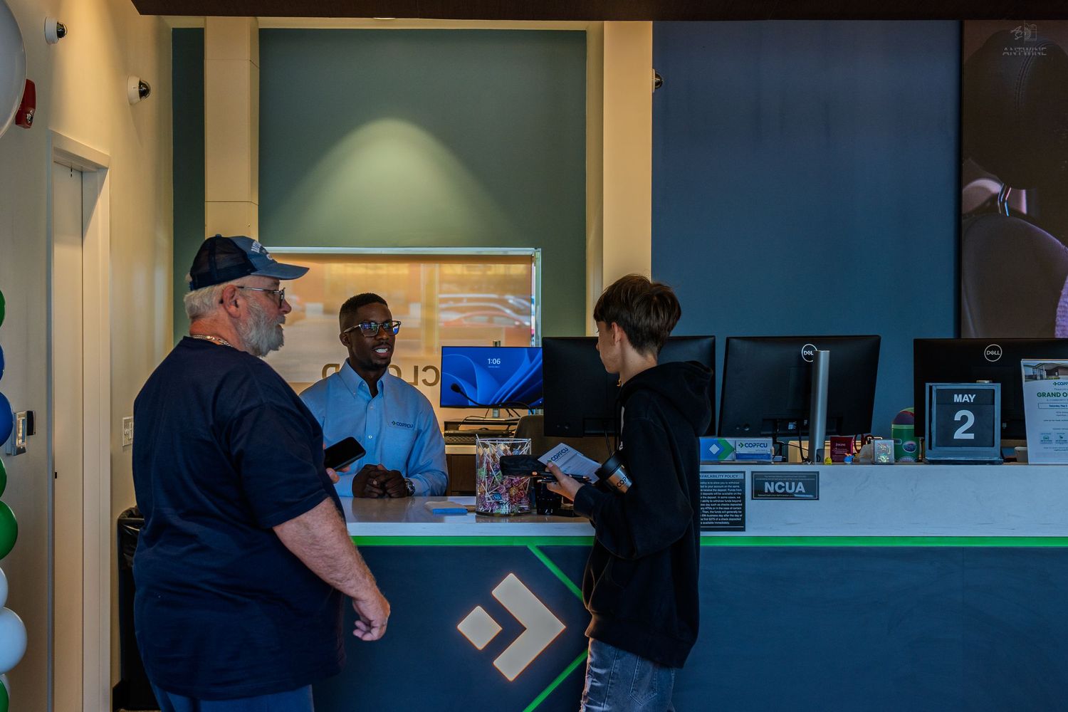 Customers interact with staff at a modern service counter with computers during a business grand opening event.