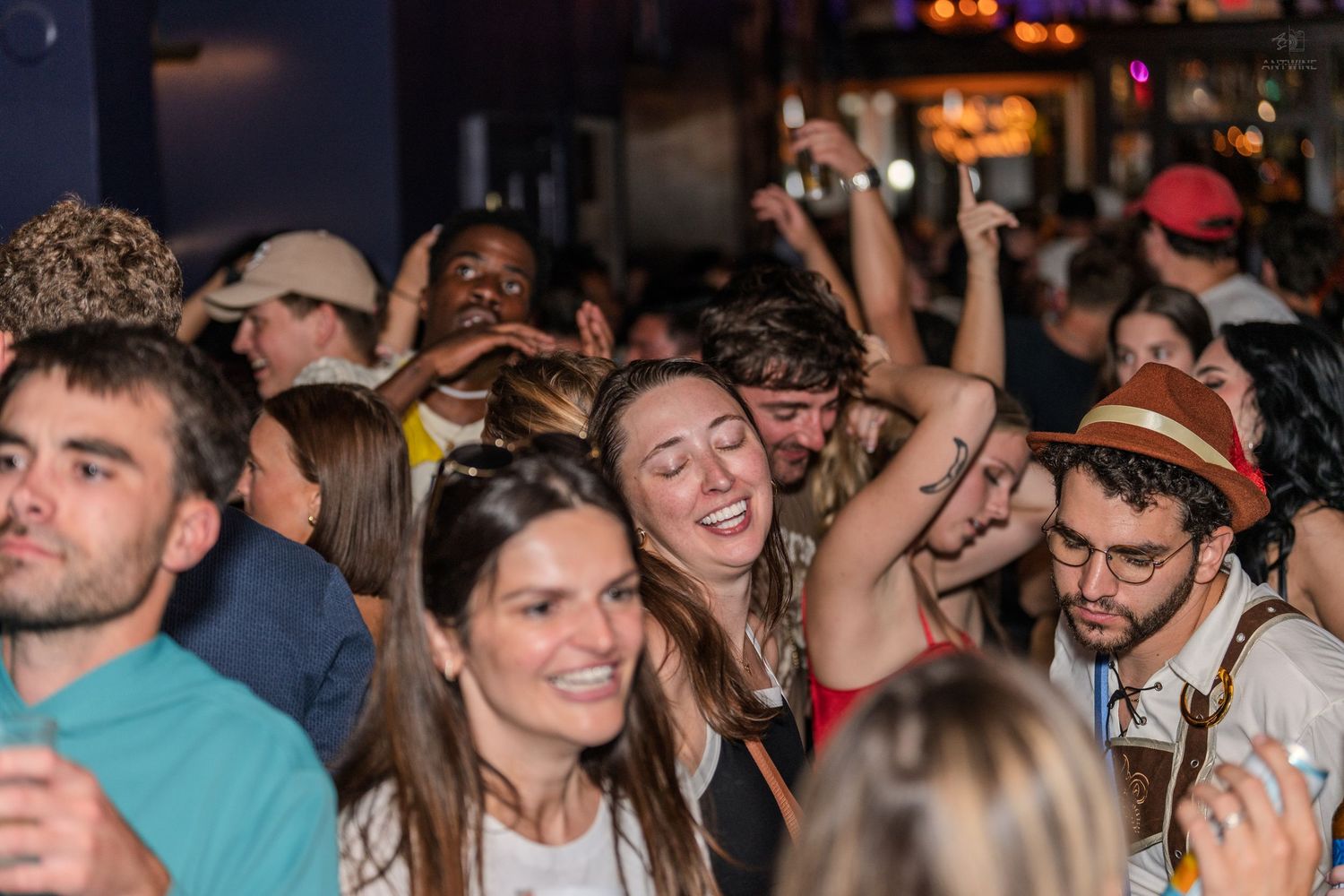 Crowd of people dancing and celebrating at a lively indoor bar or music venue event.
