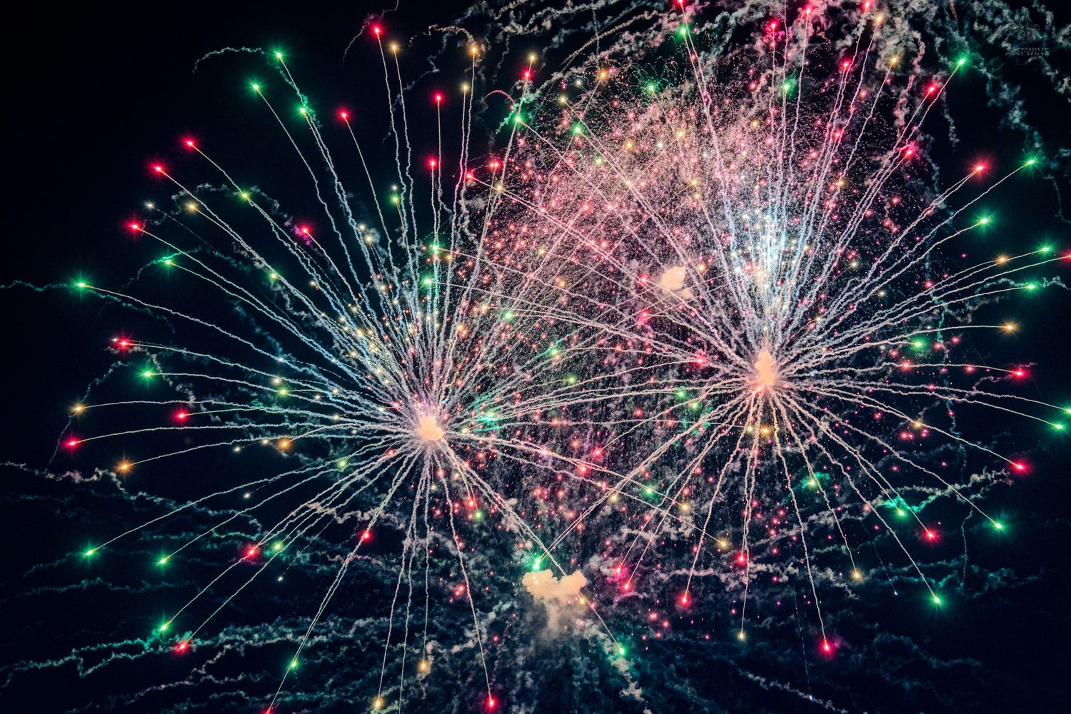 Colorful fireworks display lighting up the night sky with red, green, and pink bursts.