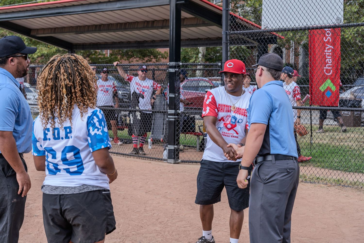 People in baseball jerseys talking with umpires near a dugout at an outdoor baseball game.