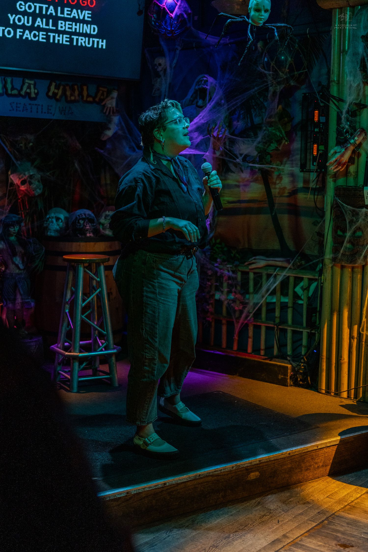 Singer performing karaoke on dimly lit Halloween-decorated stage at Hula Hula bar in Seattle, Washington.