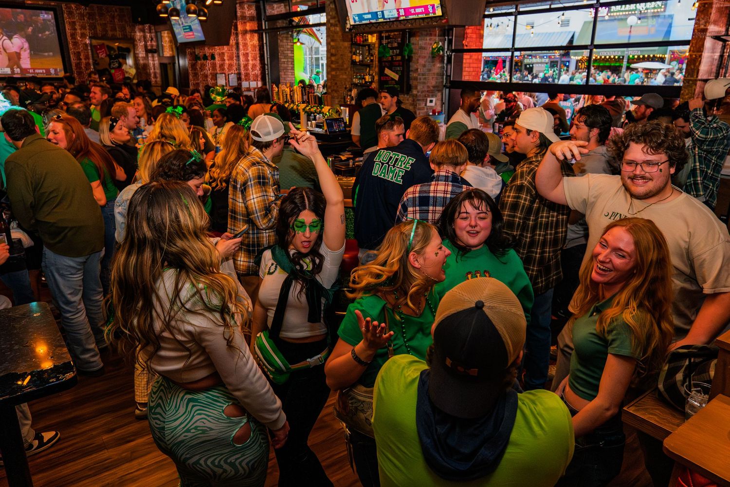 Lively St. Patrick's Day bar crowd with patrons wearing green, socializing and dancing under festive lighting.