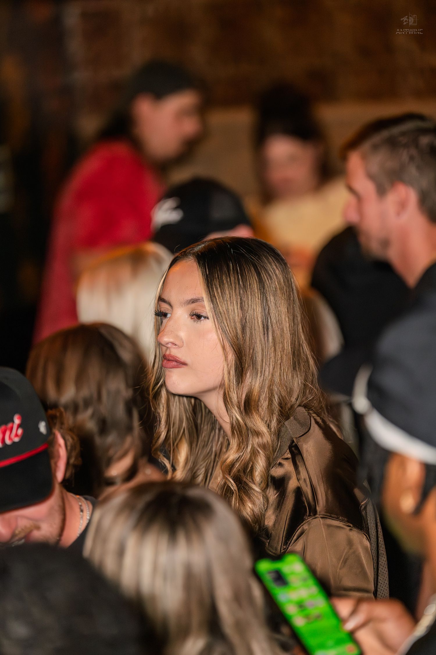 Young woman with long wavy hair standing in a crowded venue.