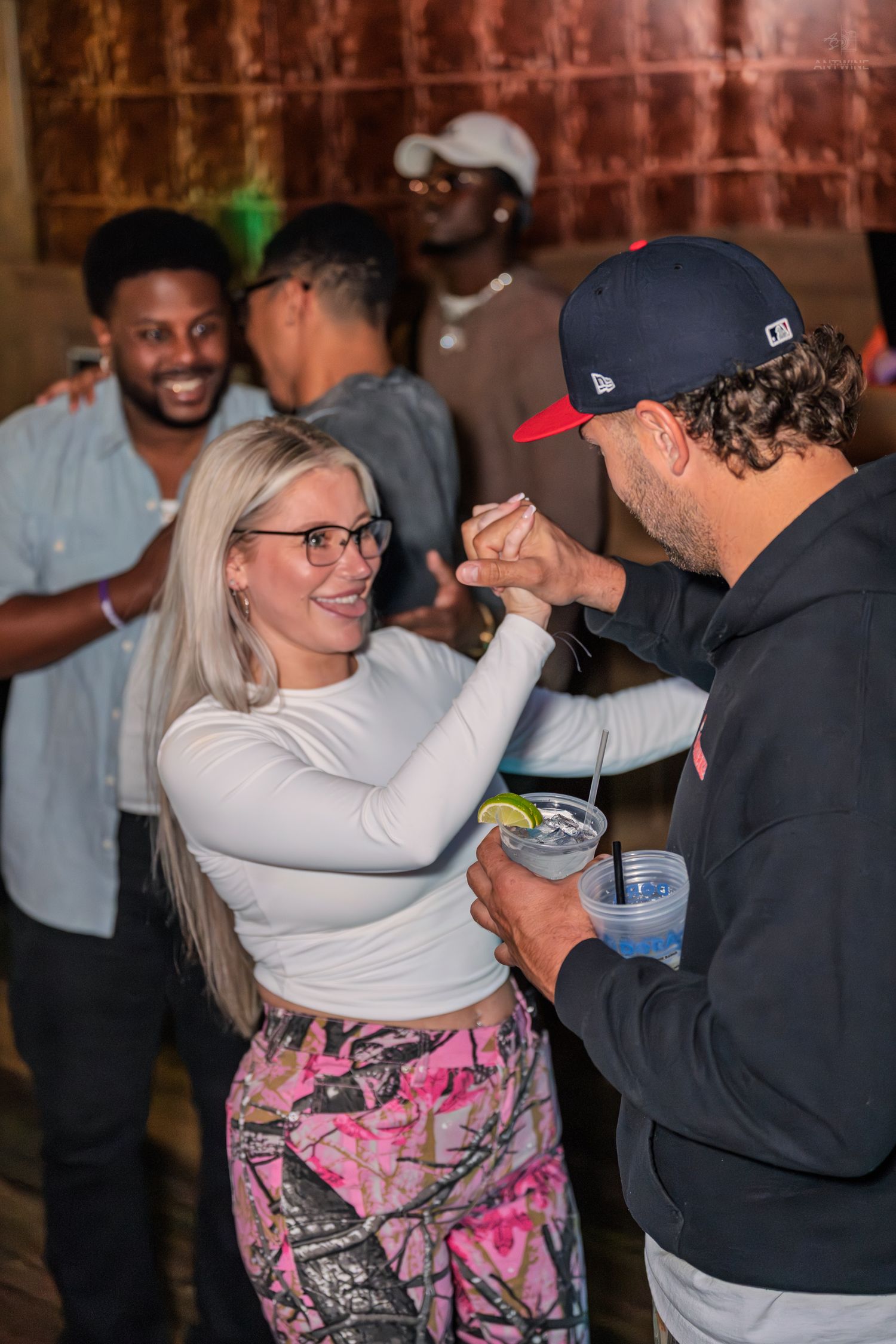 Smiling blonde woman dancing with a man holding a cocktail at a lively nightclub.