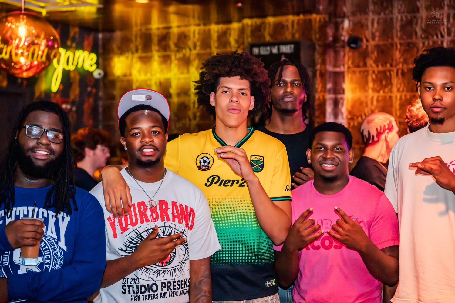 Group of six young men smiling and posing at a colorful nightclub event.
