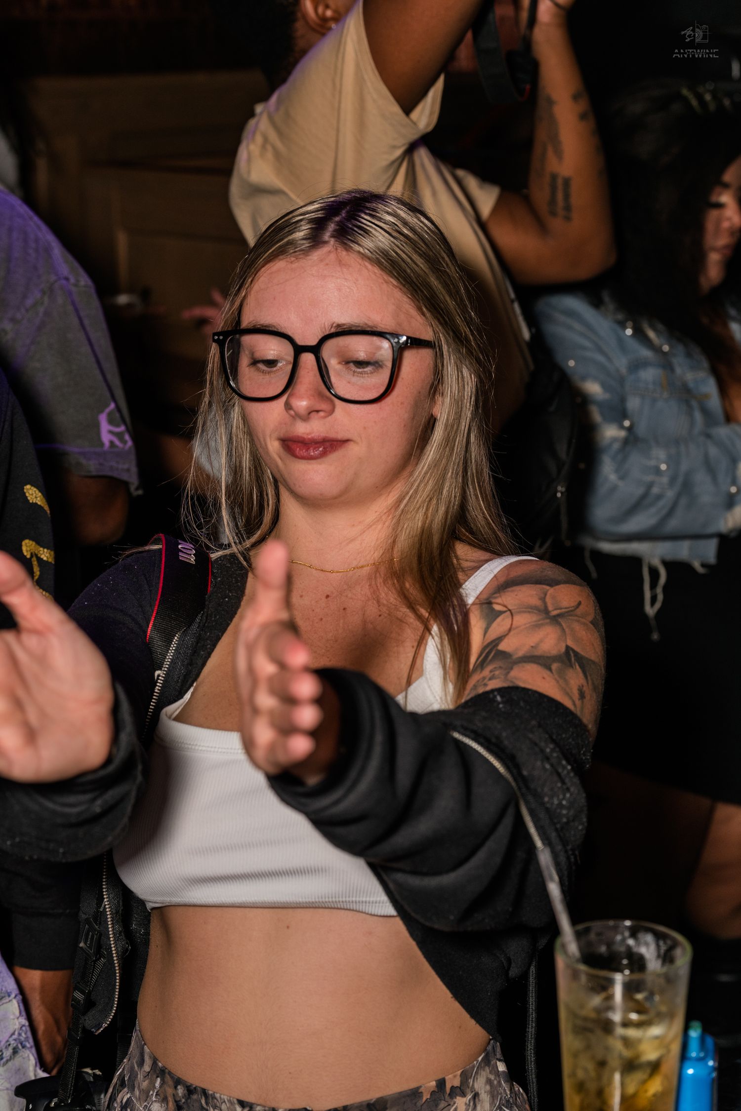 Young blonde woman with black glasses and tattoos dancing at a nightclub party.