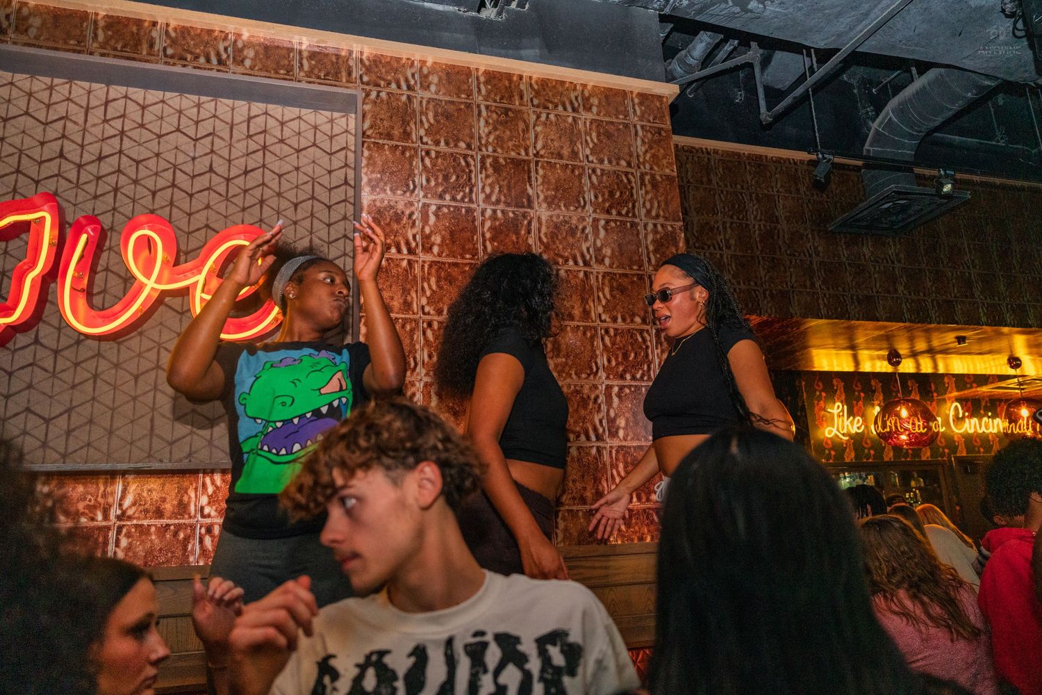 Group of people socializing and dancing near a neon sign at a nightclub.