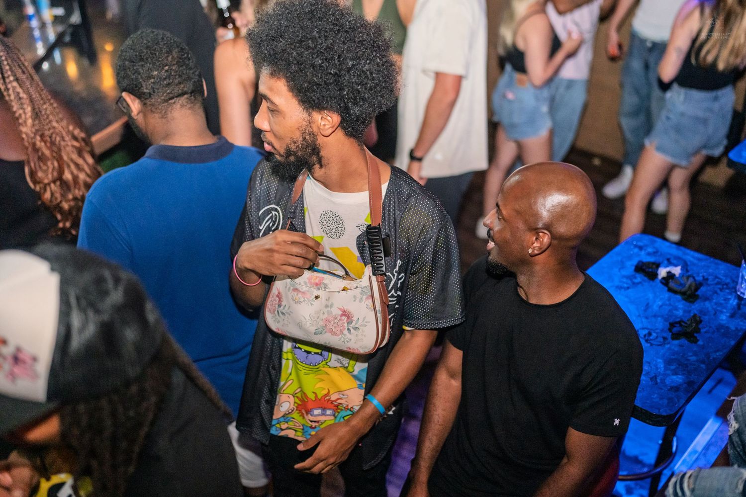 Two men having a conversation in a crowded nightclub with colorful lighting.