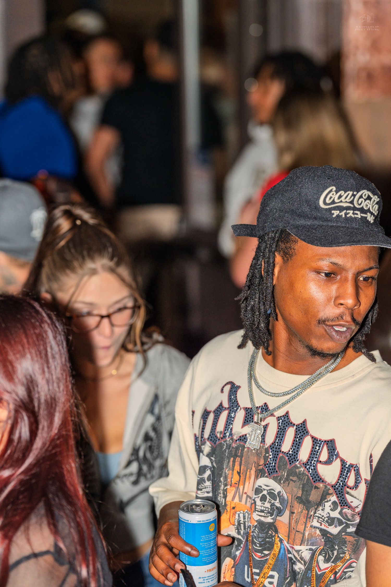 Man in a Coca-Cola cap holding a drink at a lively nightclub or bar event.