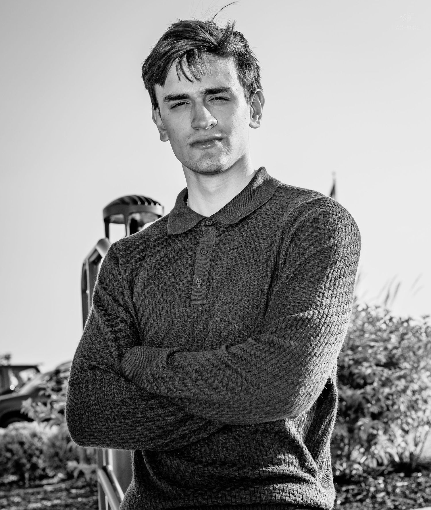 Young man with crossed arms in black and white portrait photo outdoors wearing a textured polo sweater.