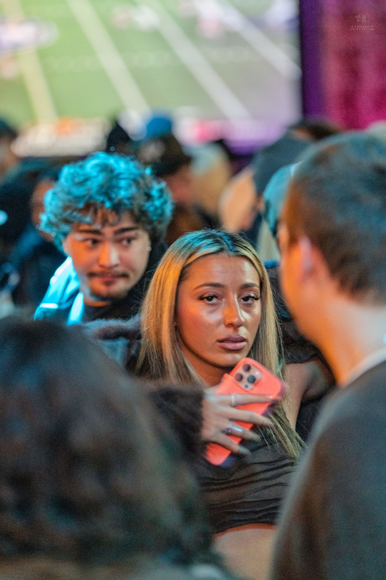 Young woman with blonde hair holds a red phone in a crowded colorful venue.