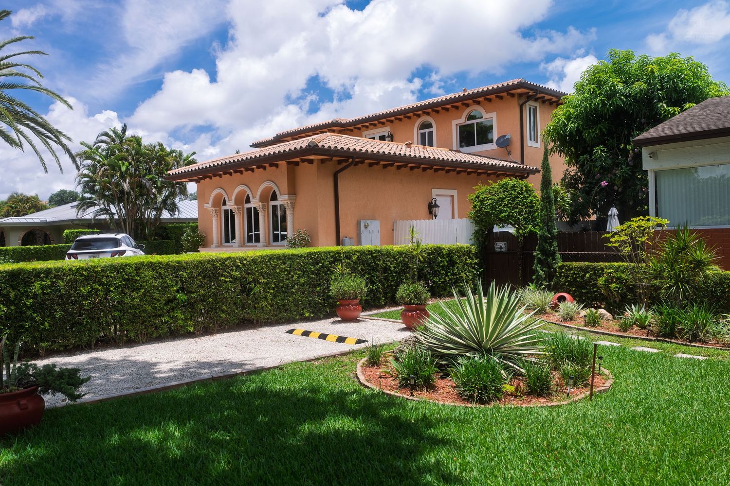 A beautiful Mediterranean-style orange stucco home with lush landscaping and a paved driveway.