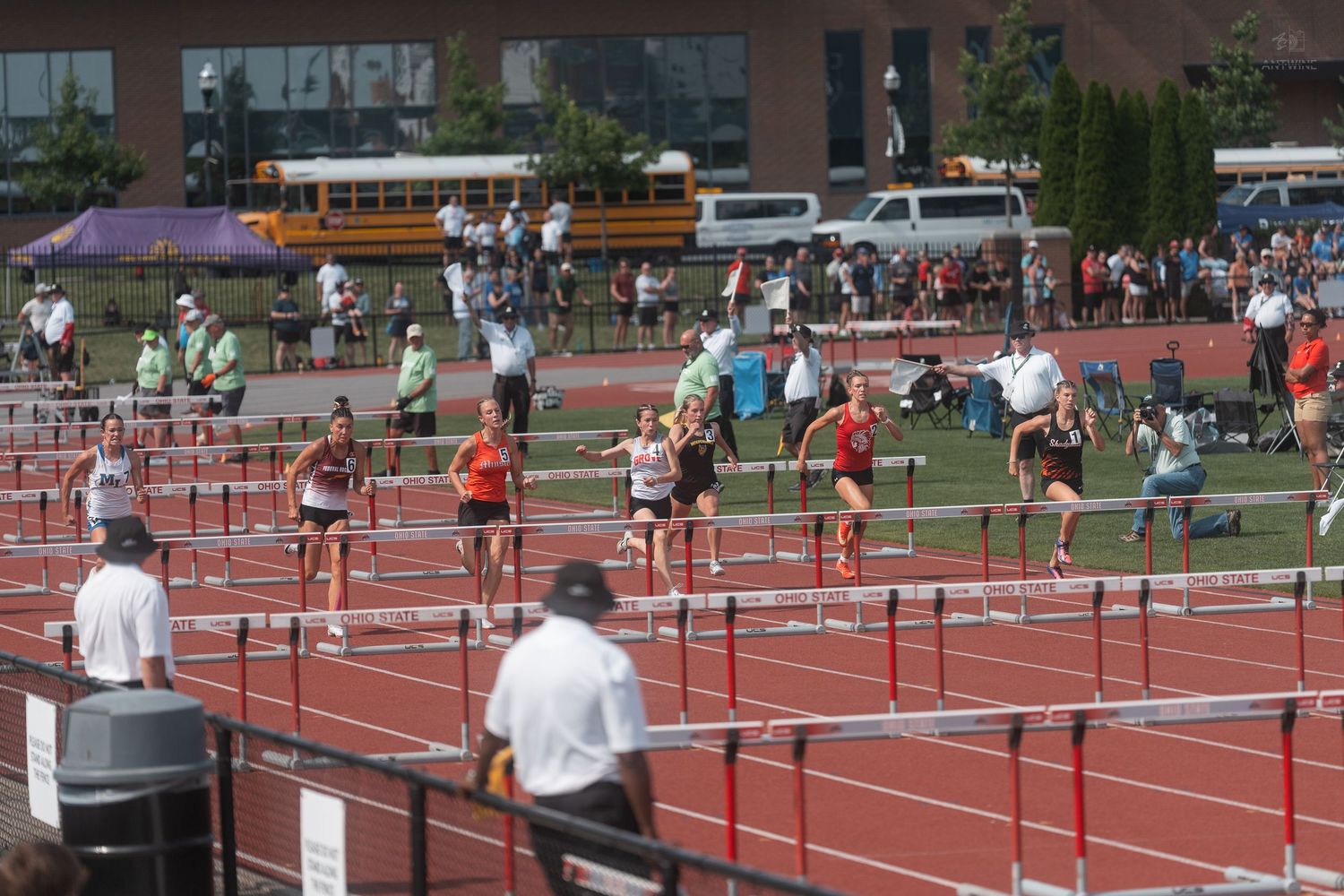 Multiple athletes clear hurdles simultaneously during competitive track and field hurdles race outdoors.