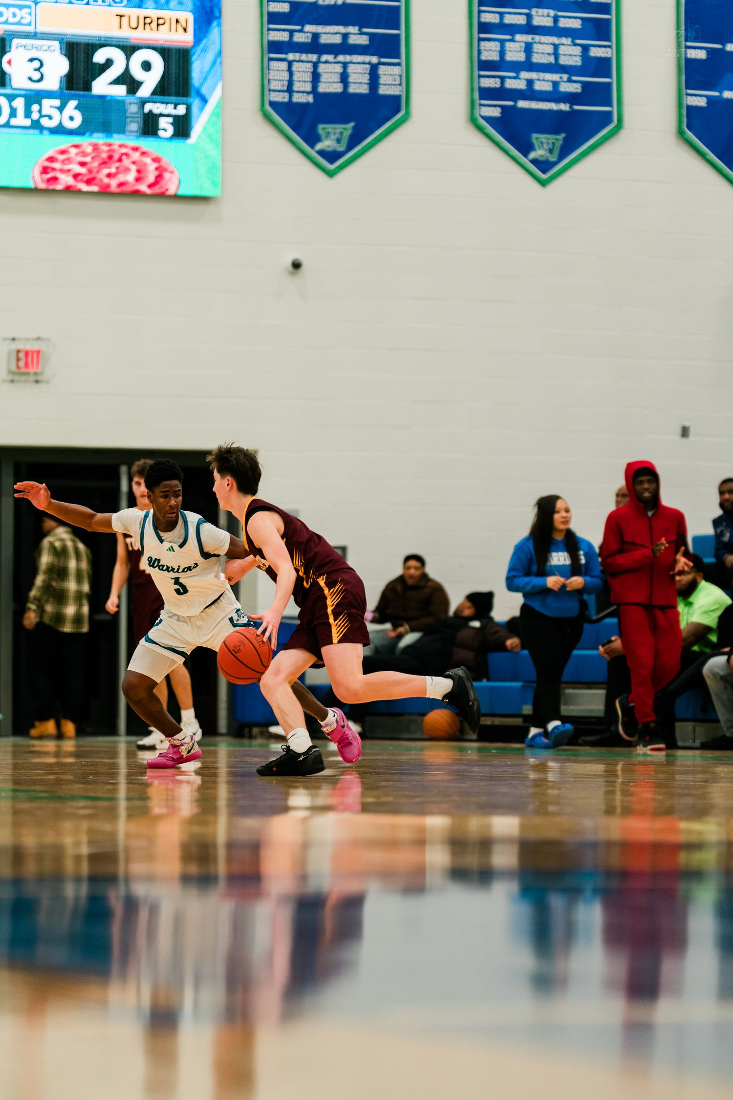 Warriors player #5 defends opponent dribbling in maroon uniform during home game.