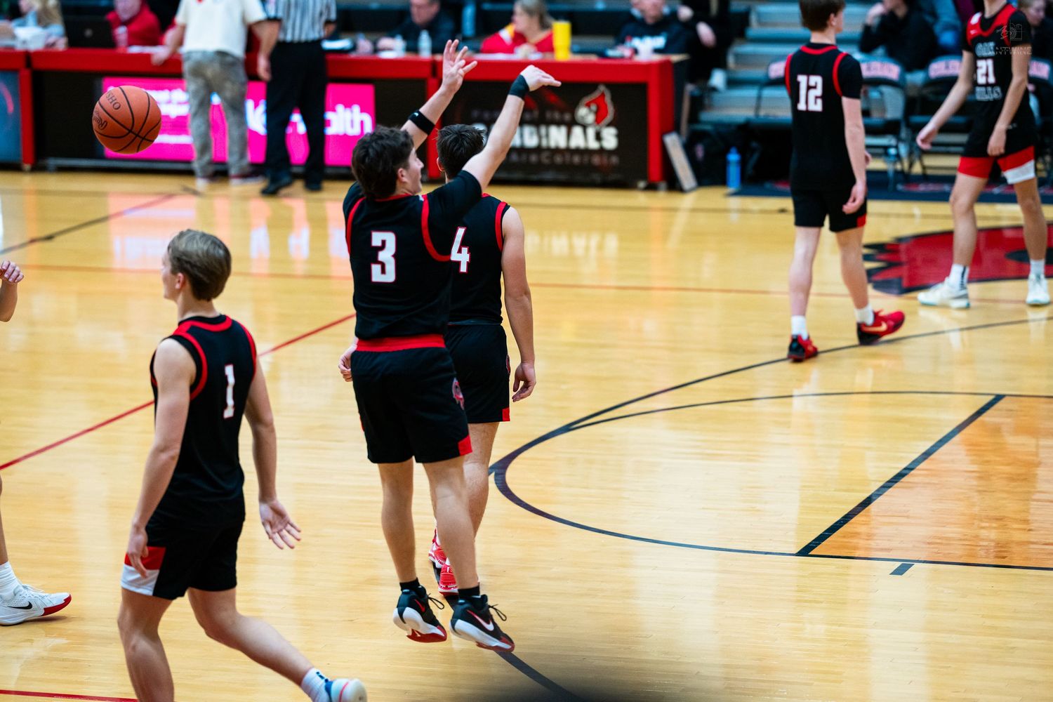 Two high school basketball players numbers 3 and 4 high-five during a game in a red gymnasium.