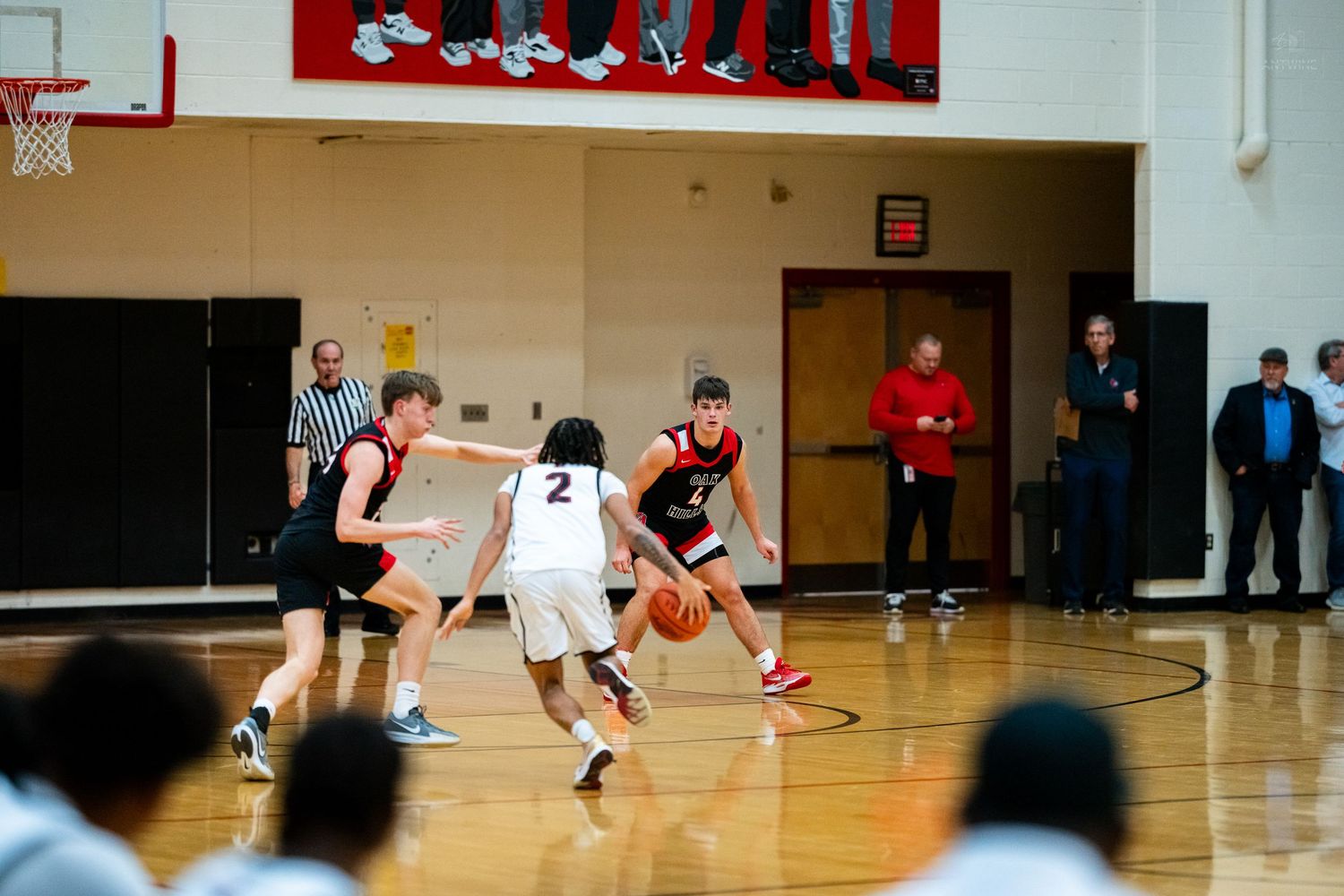 High school basketball players compete on indoor court with spectators watching from the sidelines during a game.