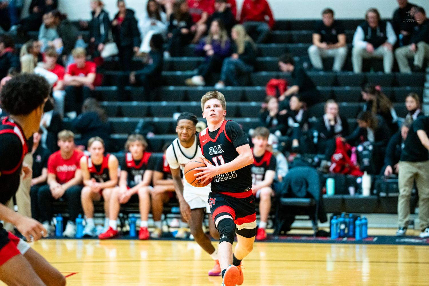 A basketball player in red and black uniform dribbles toward the basket during a high school game.