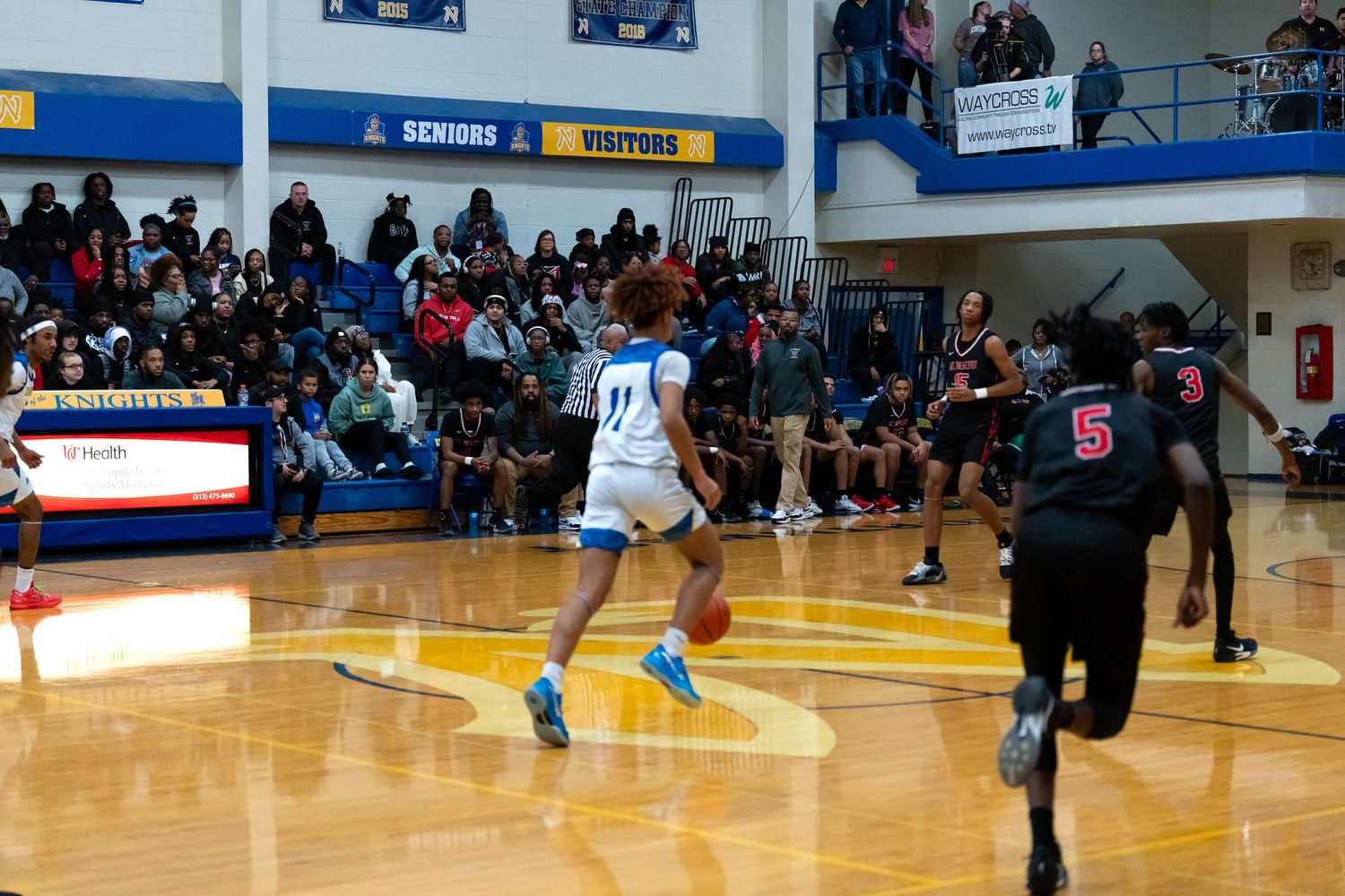 Player #11 leaps with basketball as defender #5 approaches during game.