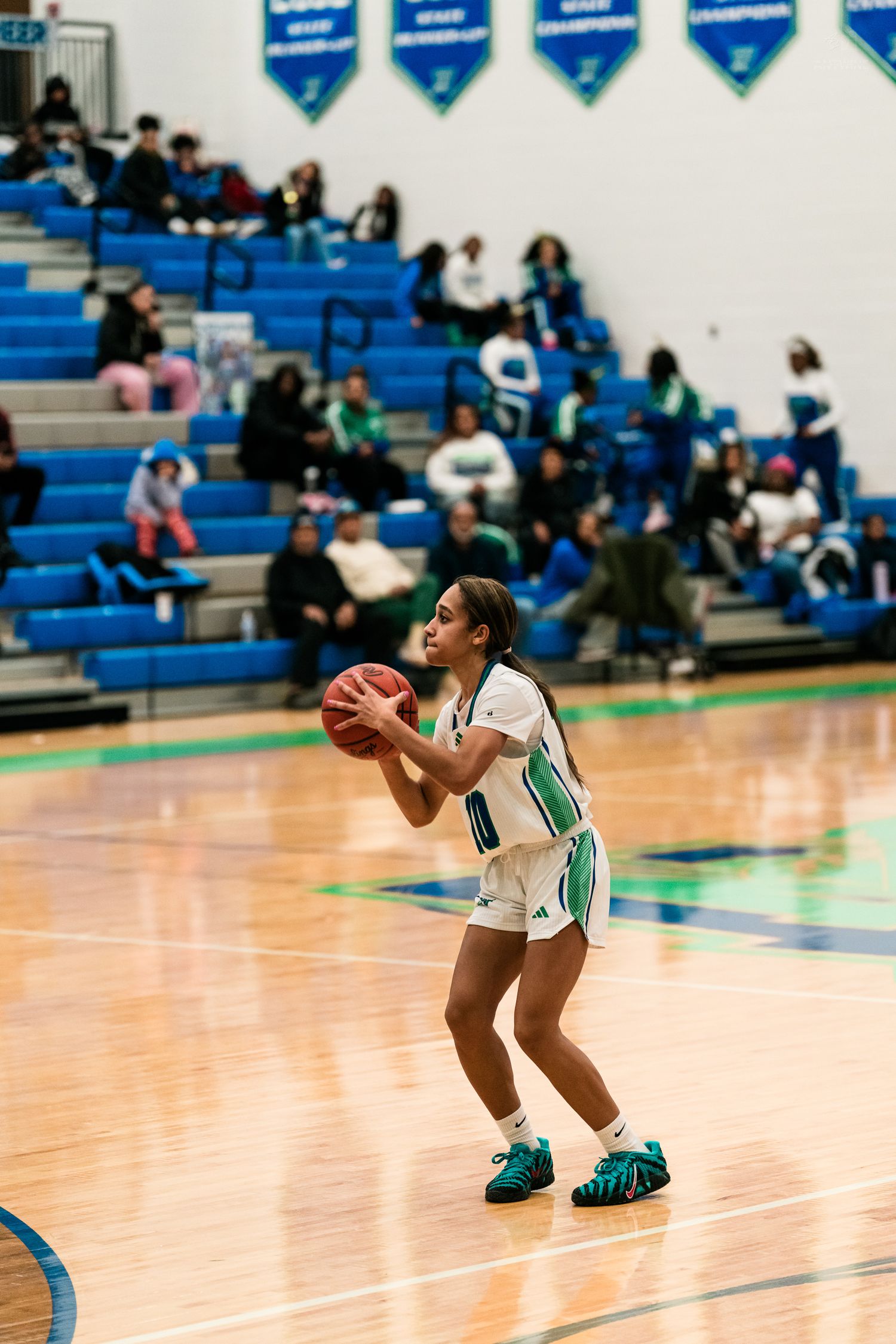 Warriors #10 sets up for a free throw shot in blue and green gymnasium with championship banners in background.