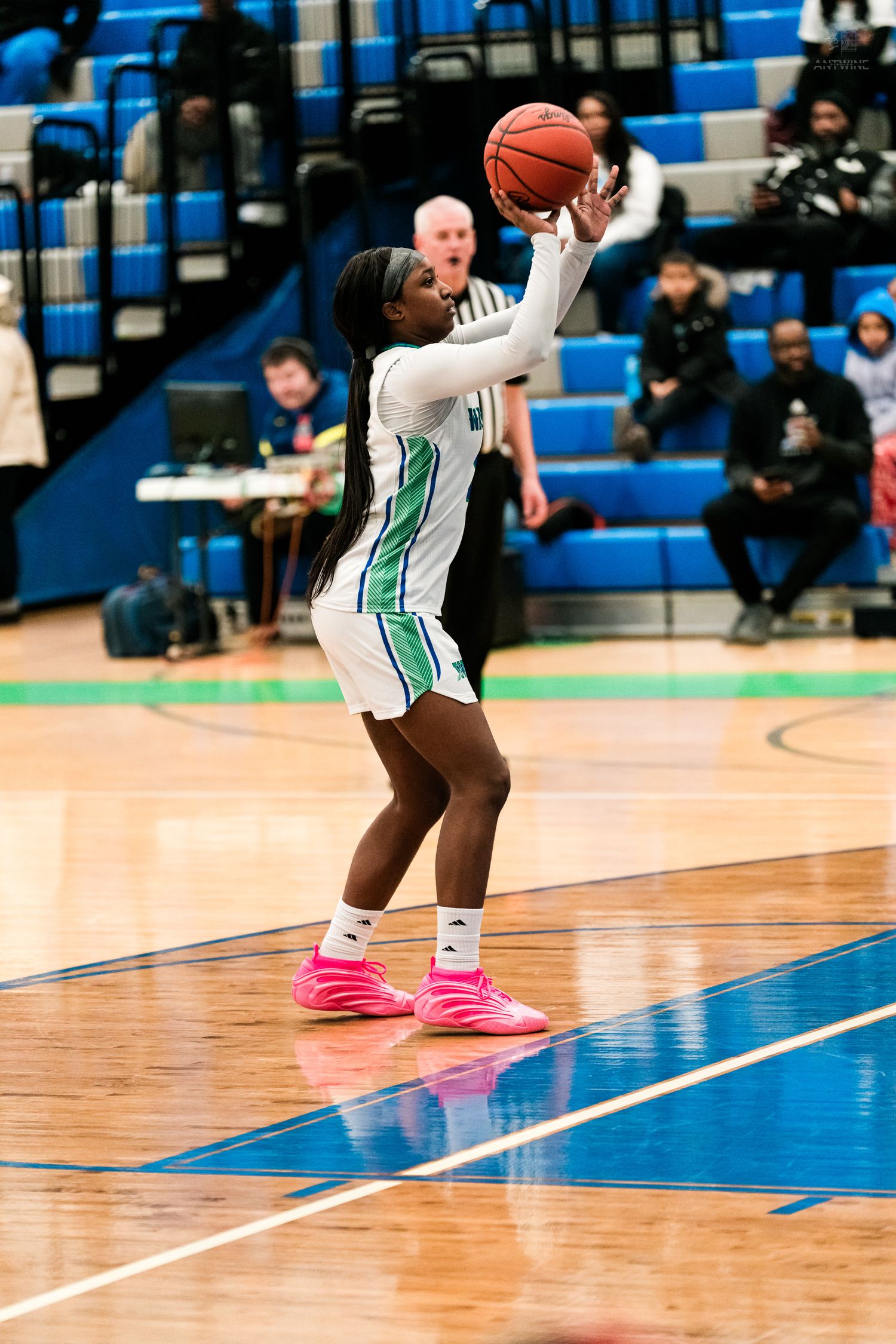 A female Warriors basketball player in white shoots the ball wearing bright pink sneakers during an indoor game.