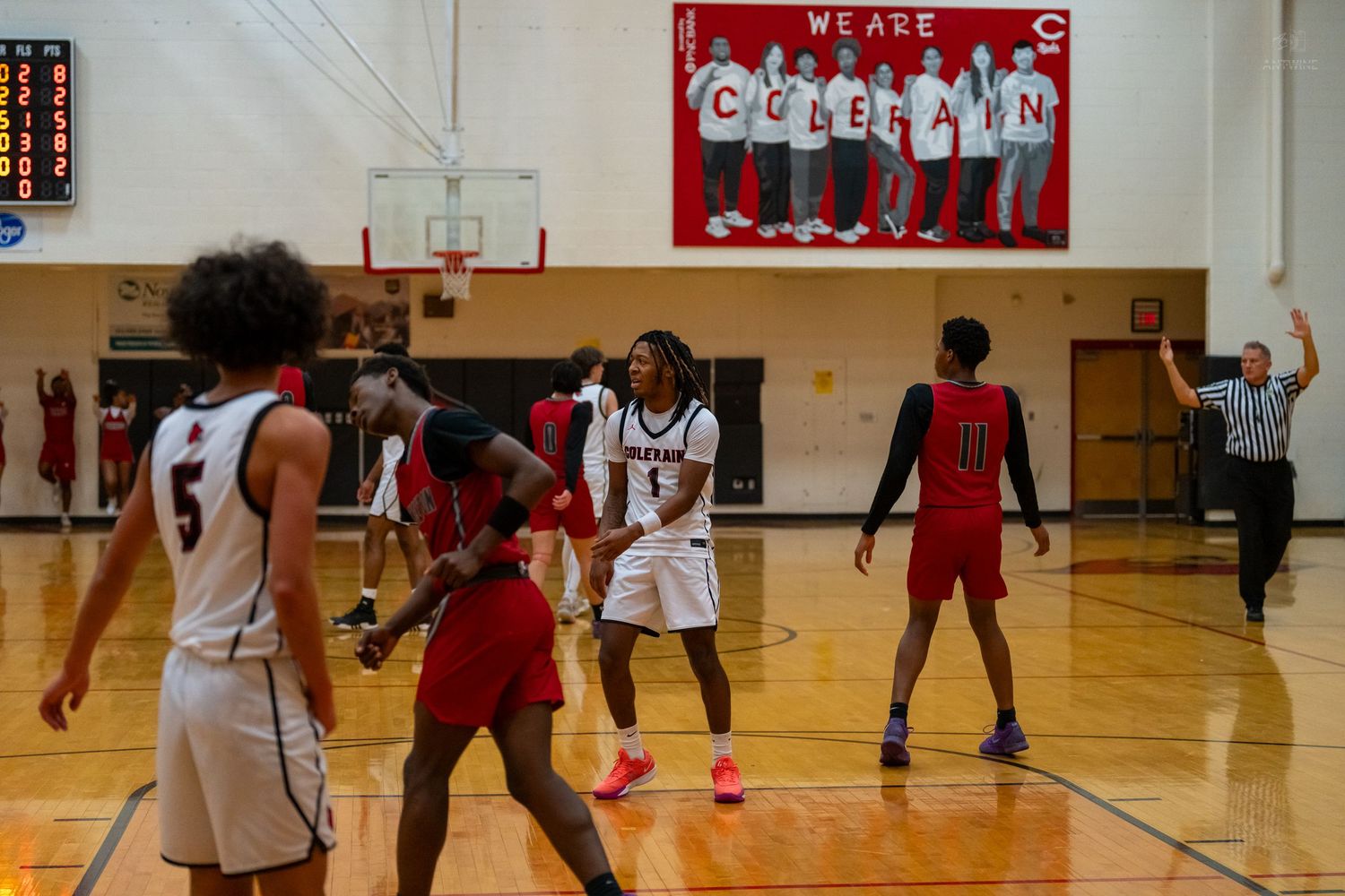 High school basketball players celebrate on the court beneath a We Are Coleman banner during a game.