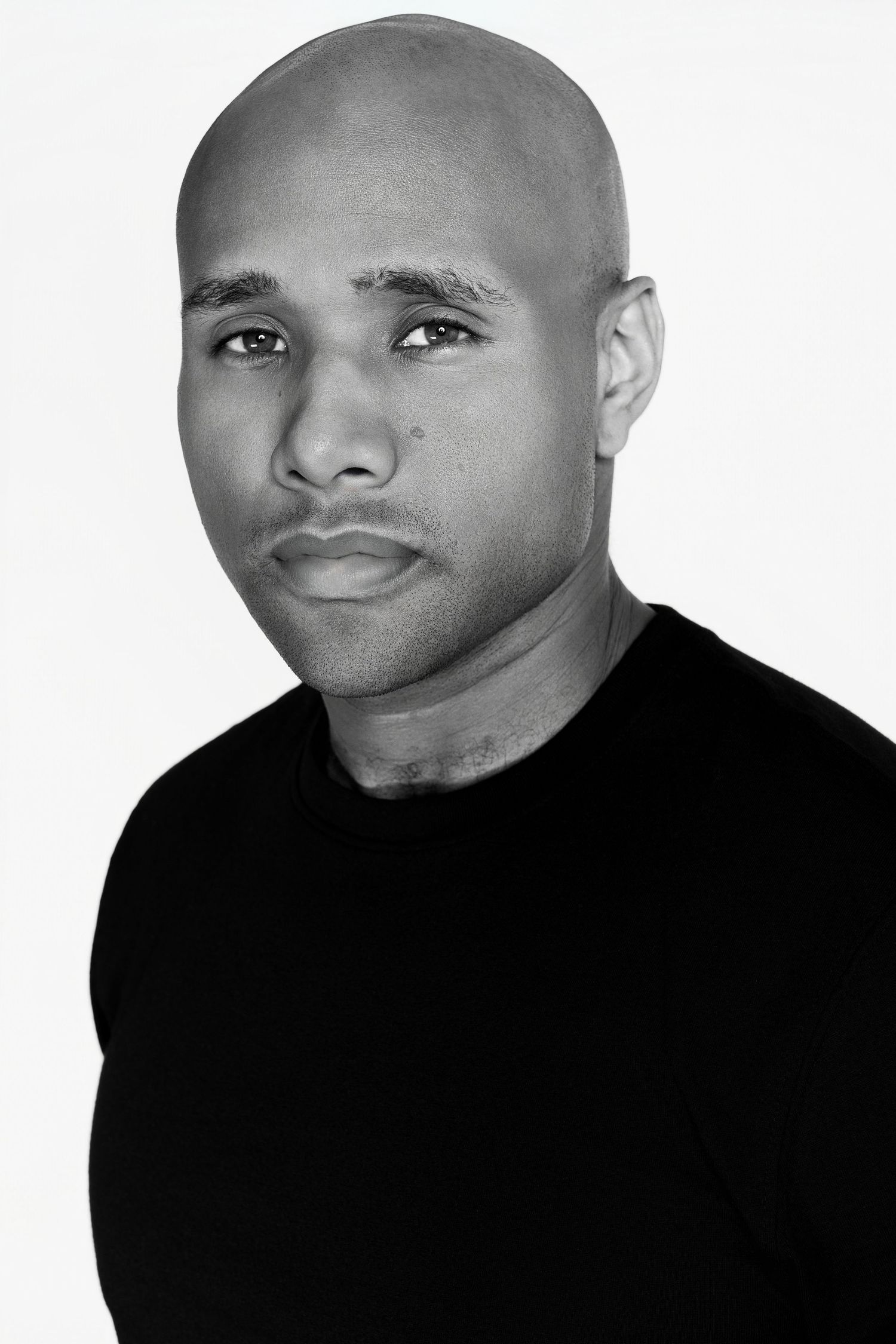 Black and white headshot of bald man in black t-shirt against white background.