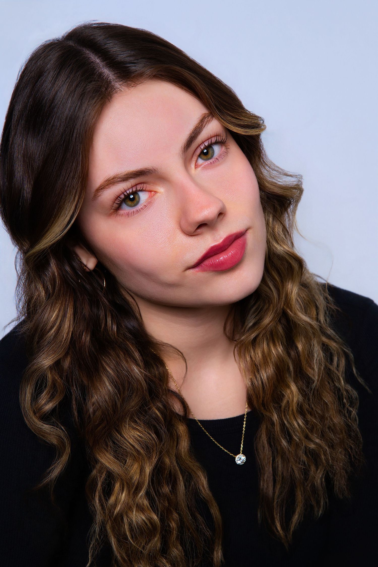 Young woman with curly brown hair and bold red lips poses for a portrait with colorful eye makeup.