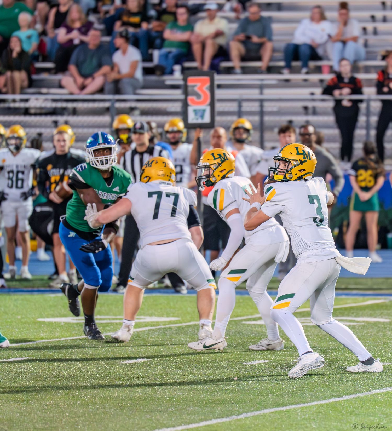 High school football offensive line blocks as quarterback prepares to hand off during game.