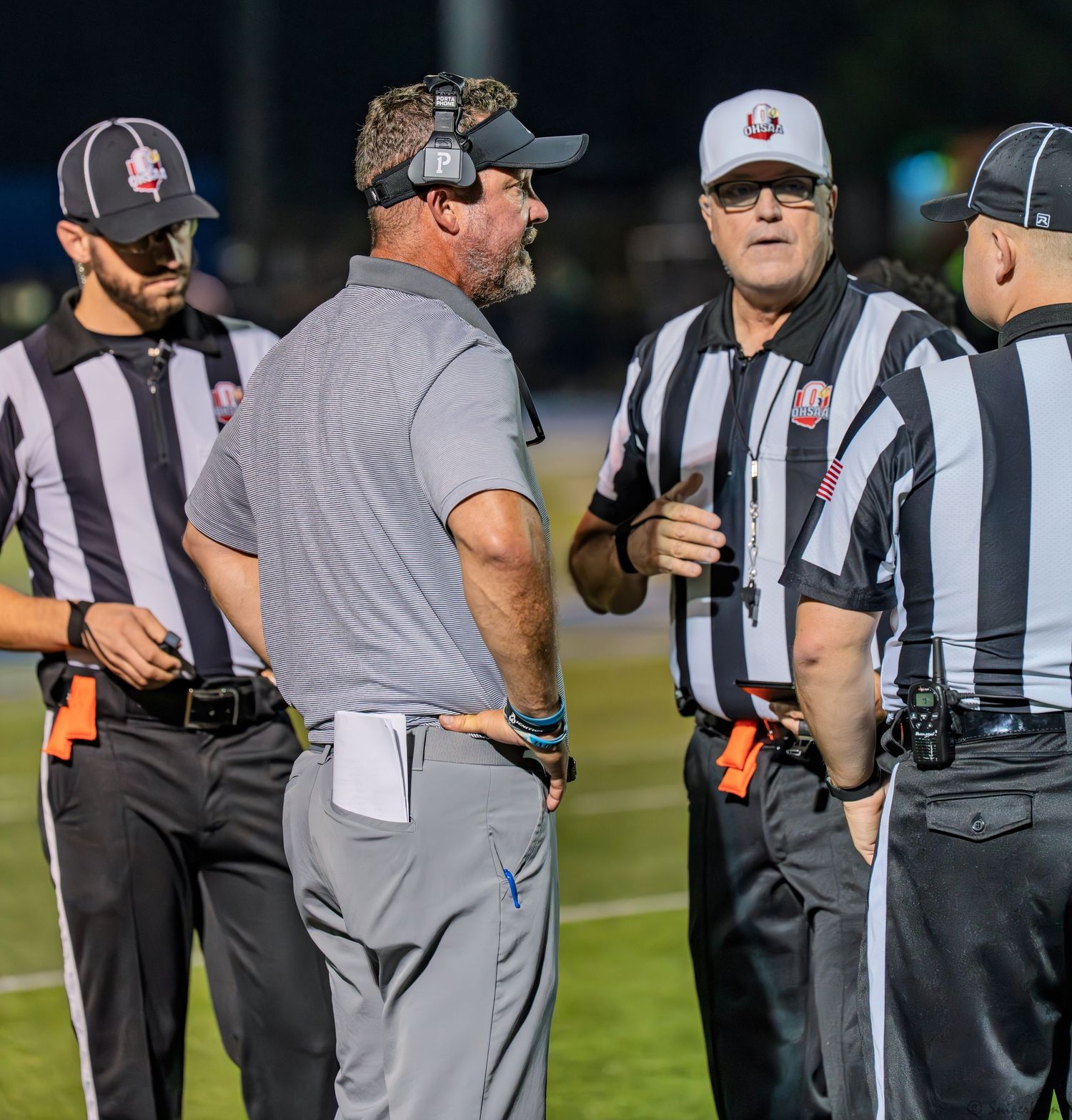 Warriors head coach in gray discusses a call with three referees in black and white stripes.