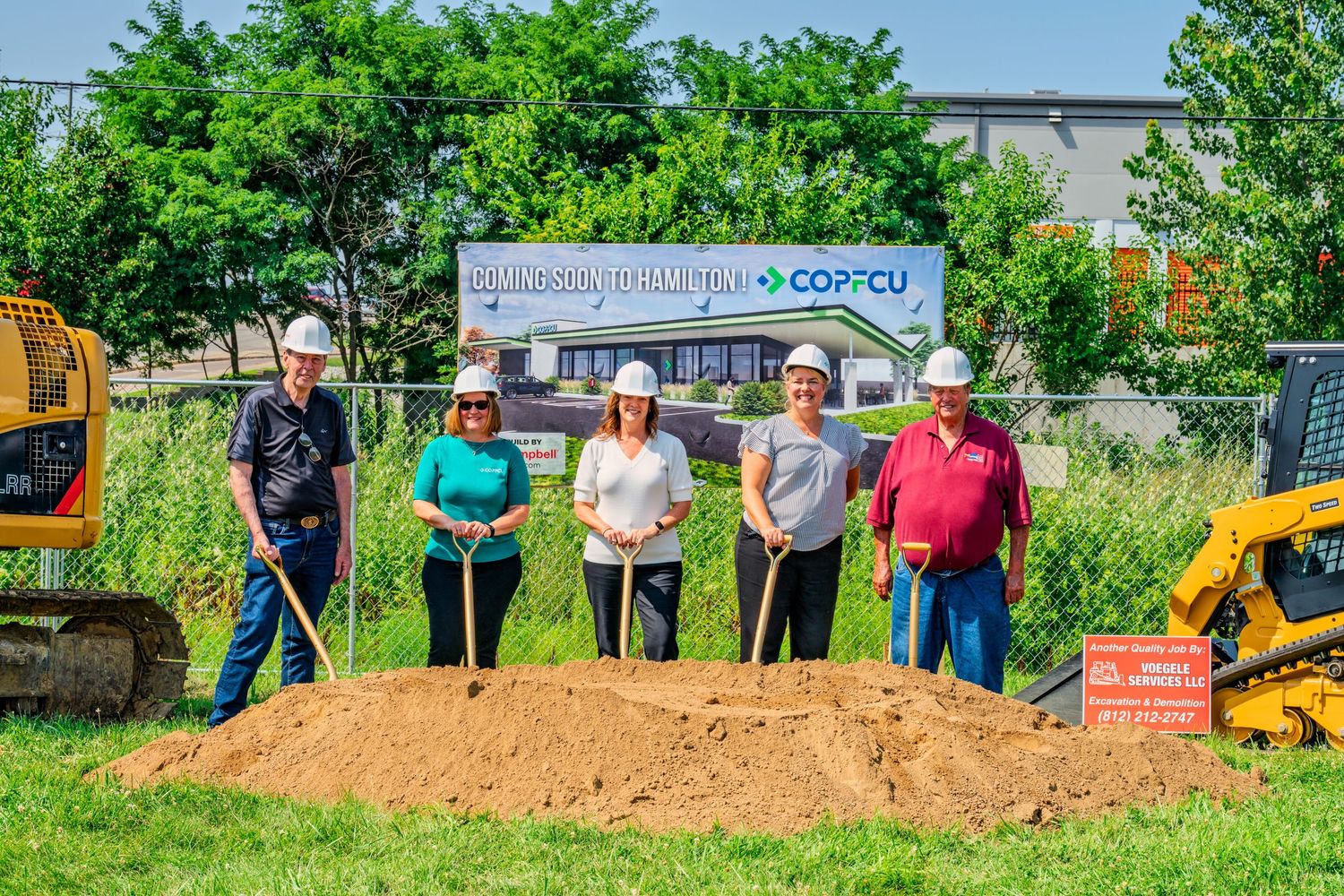 Five smiling people in hard hats with shovels at COPFCU Hamilton branch groundbreaking site.