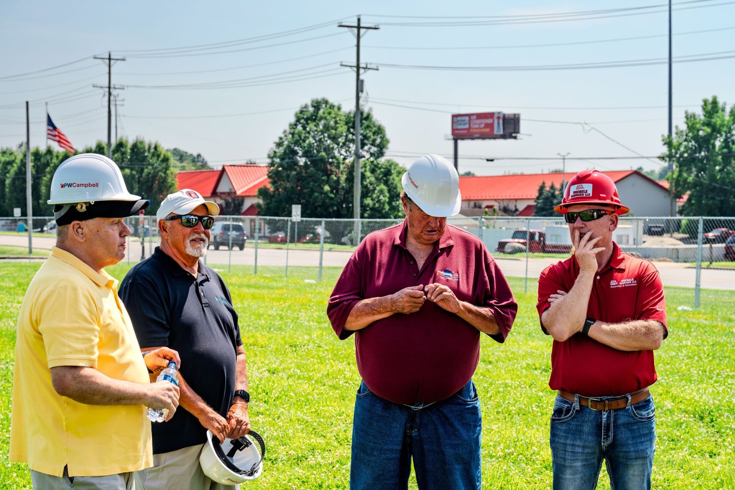 Four men in hard hats converse at COPFCU Hamilton groundbreaking construction site outdoors.