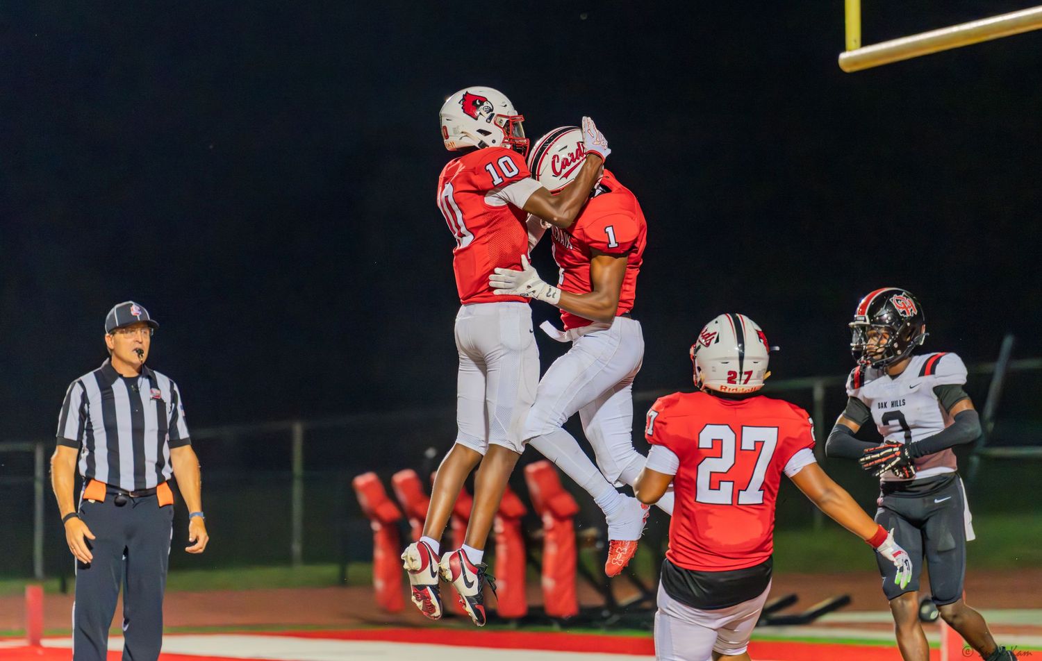 Two high school football players celebrate touchdown with chest bump near end zone.