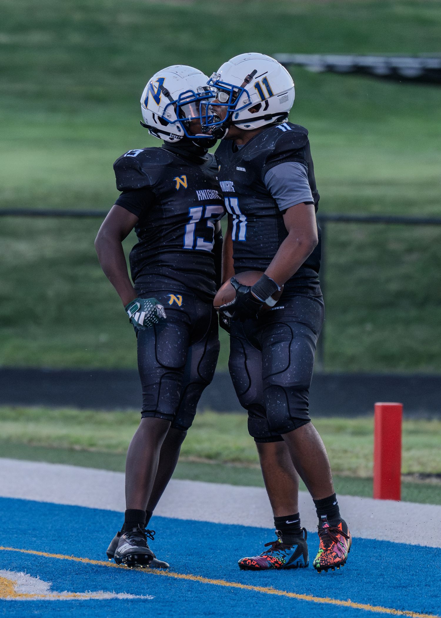 Two high school football players in black Knights uniforms celebrate together in the end zone after a touchdown.