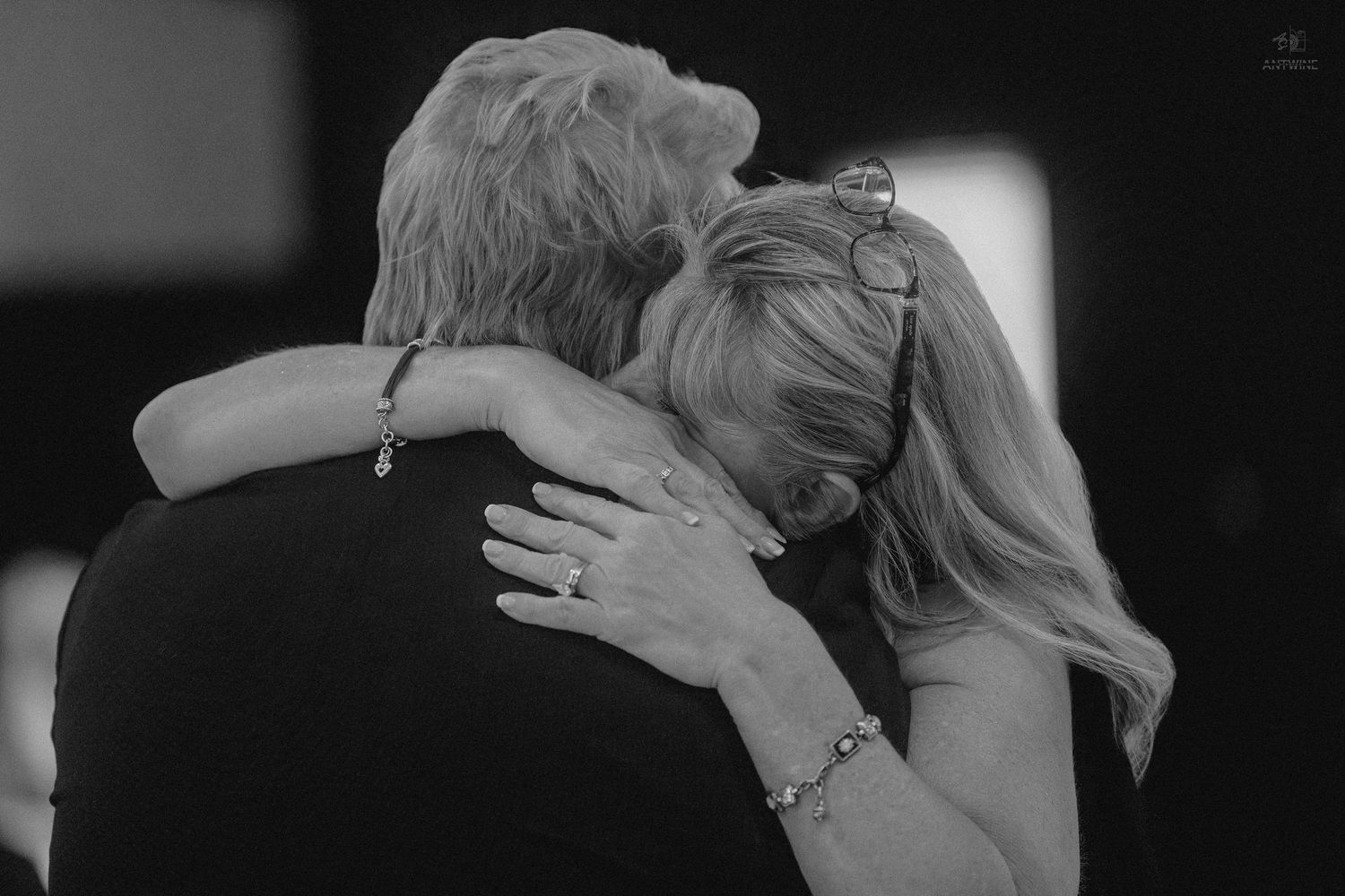 Black and white photo of two women sharing an emotional embrace at a wedding reception.