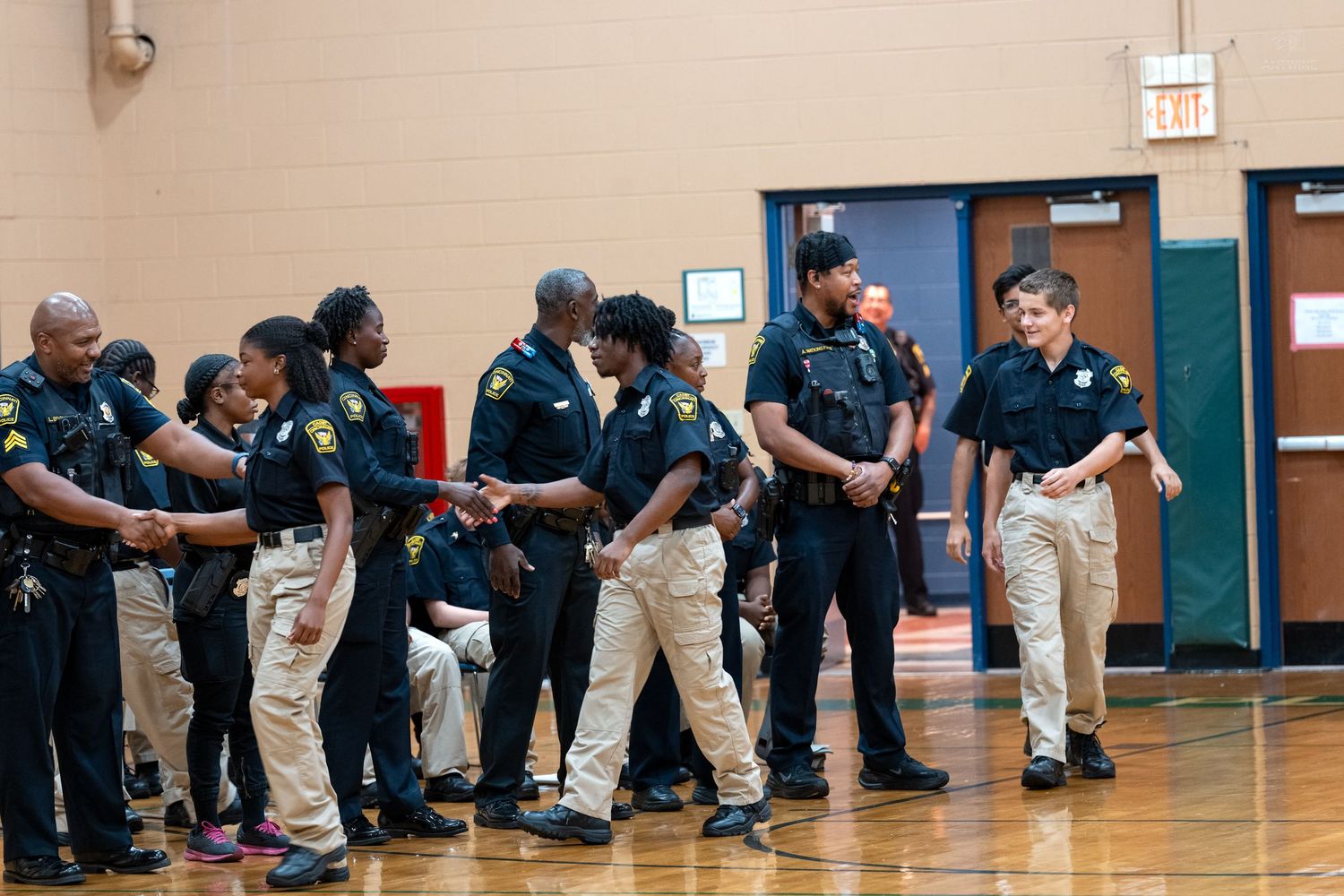 Police officers in uniform shaking hands and greeting each other in a school gymnasium.