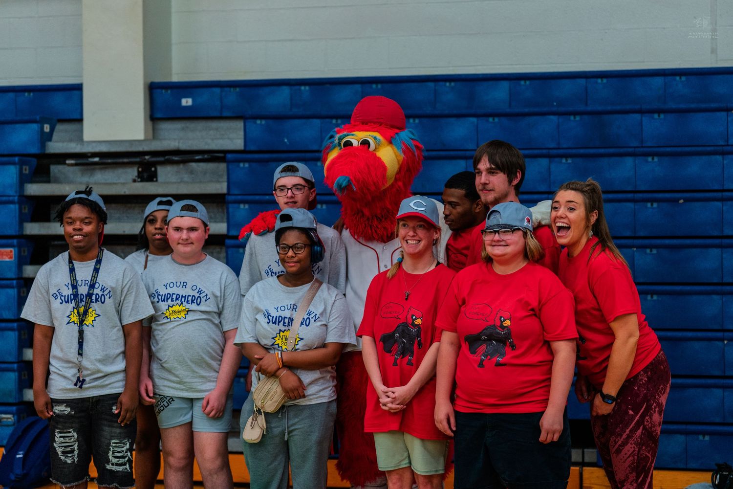 Group of students in red and gray shirts posing with a cardinal mascot in a school gymnasium.