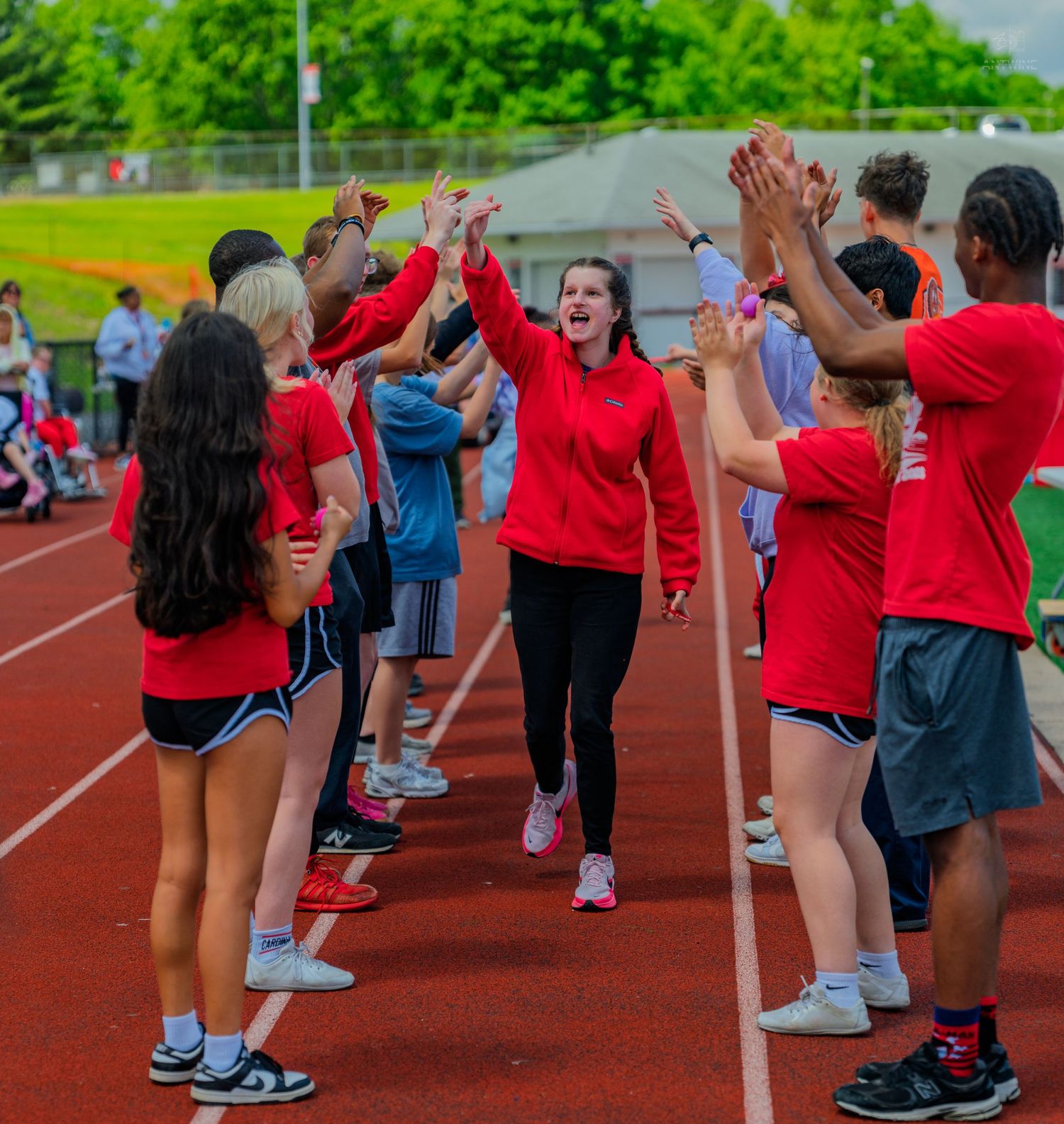 Students in red shirts high-five a woman walking through a celebratory tunnel on a track field.