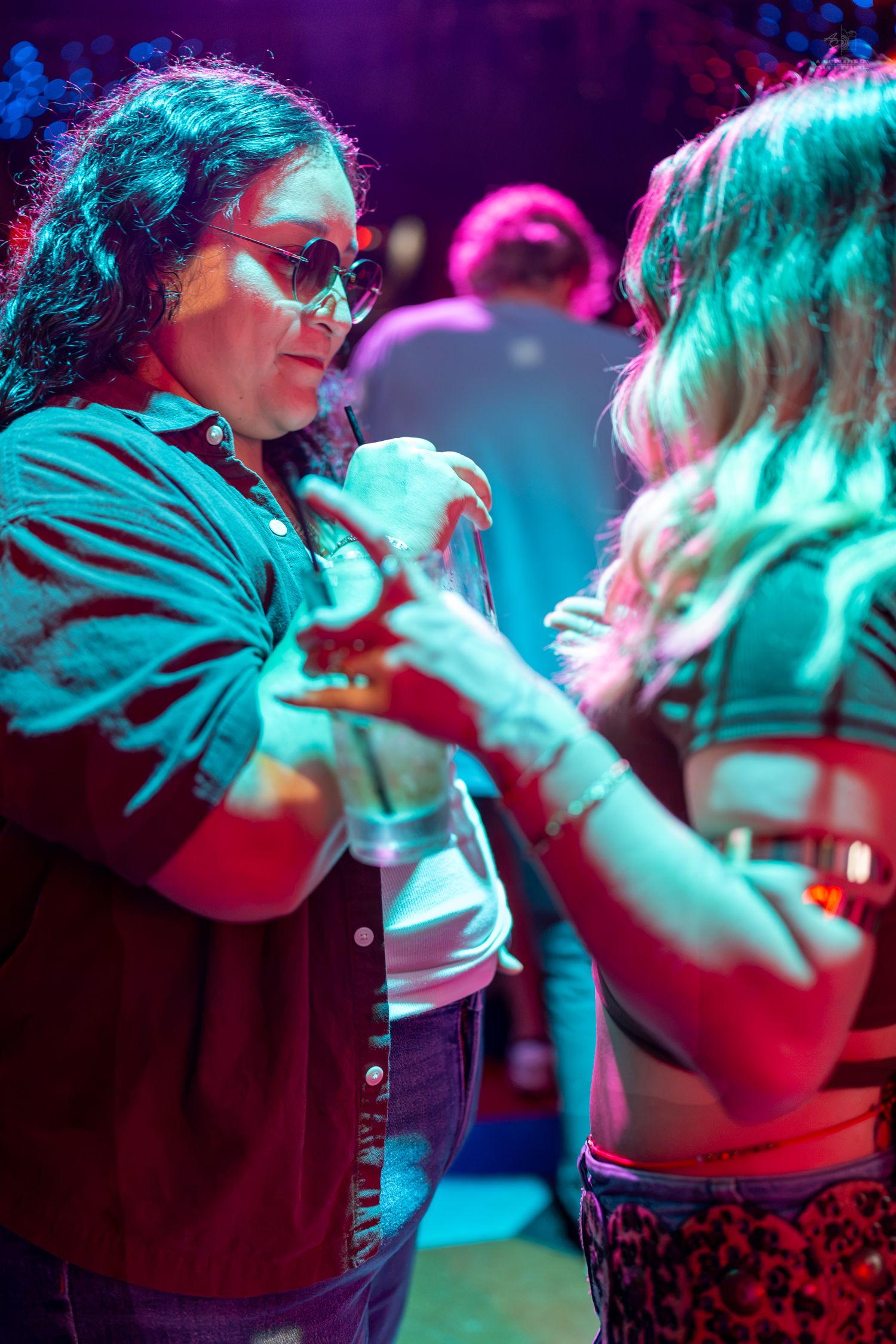 Two women dancing together under colorful neon lights at a nightclub party.