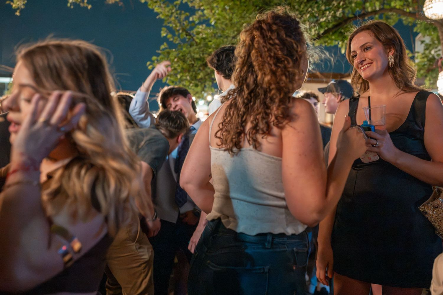 Group of young adults dancing and socializing outdoors at a nighttime party event.