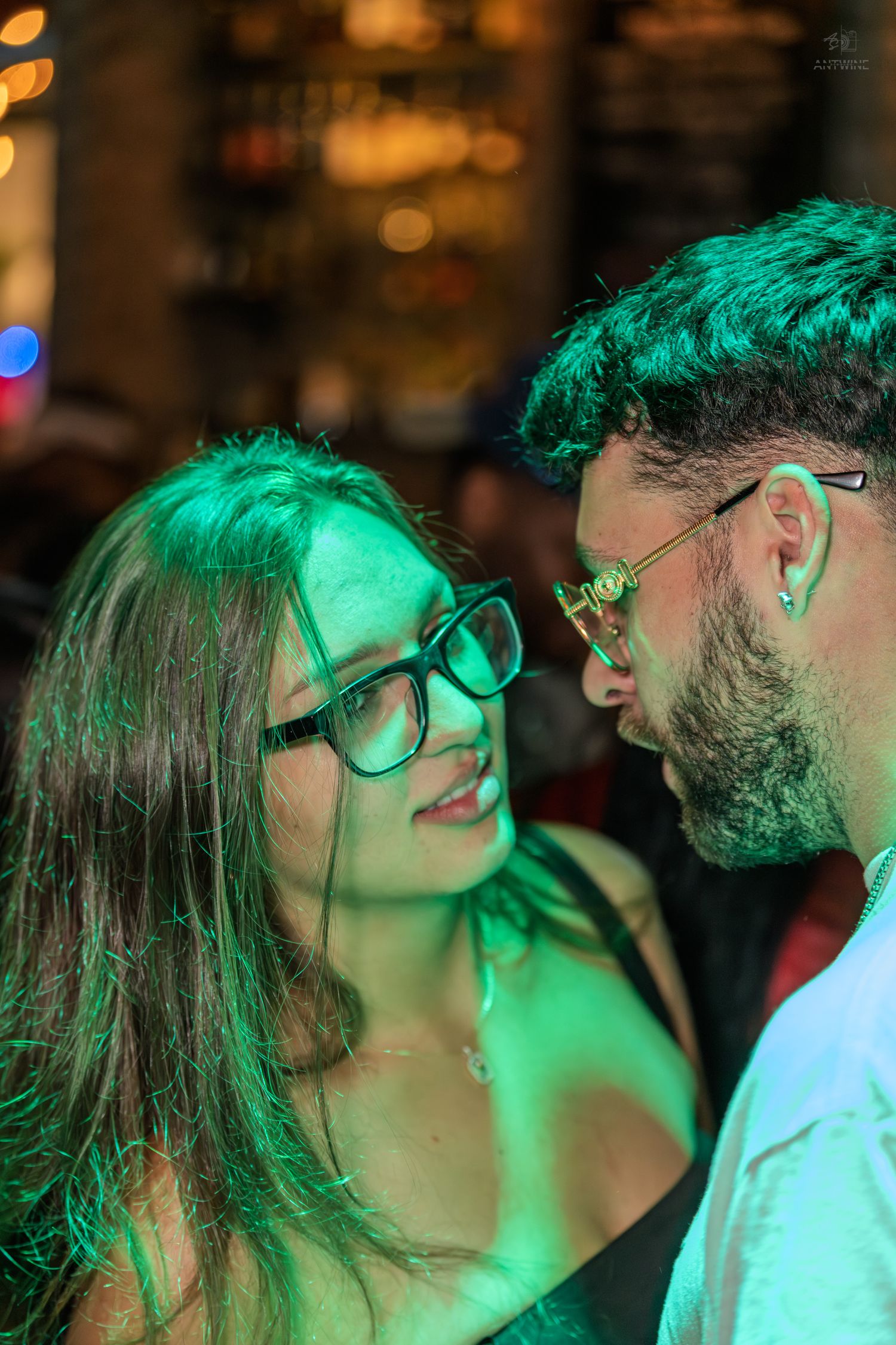 Couple sharing an intimate moment under green lights at a nightclub or bar.