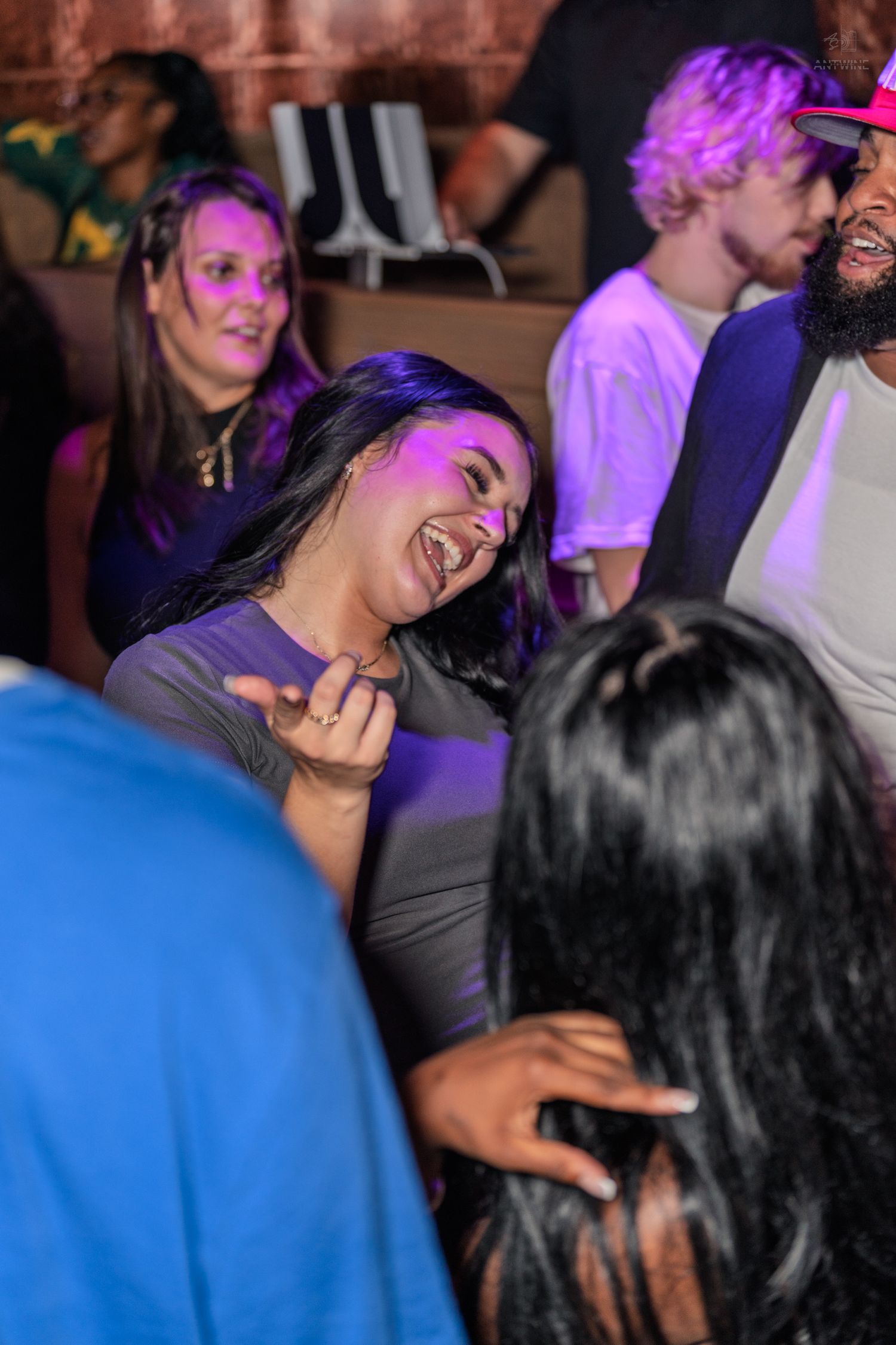 Woman laughing and dancing under purple lights in a crowded nightclub dance floor.
