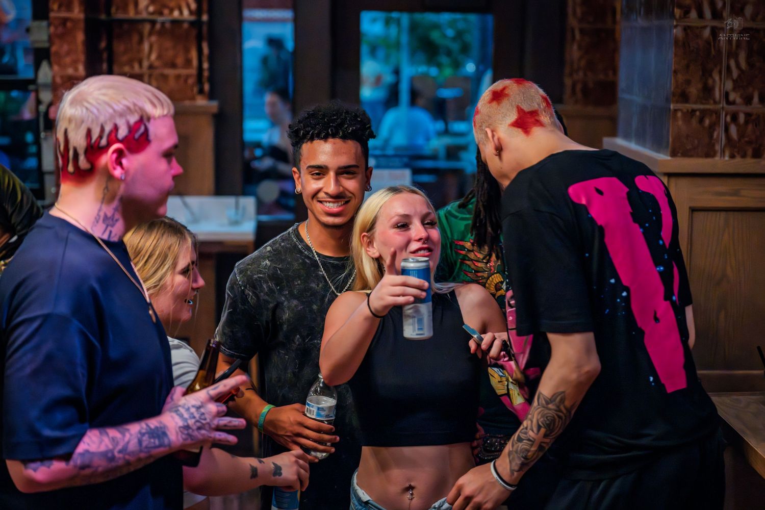 Young adults laughing and socializing at a lively indoor bar event with colorful lighting.