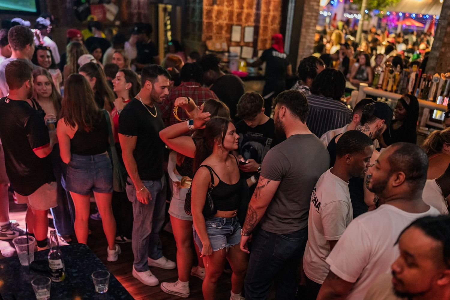 Energetic nightclub crowd with people dancing and socializing under red ambient lighting at a bar.
