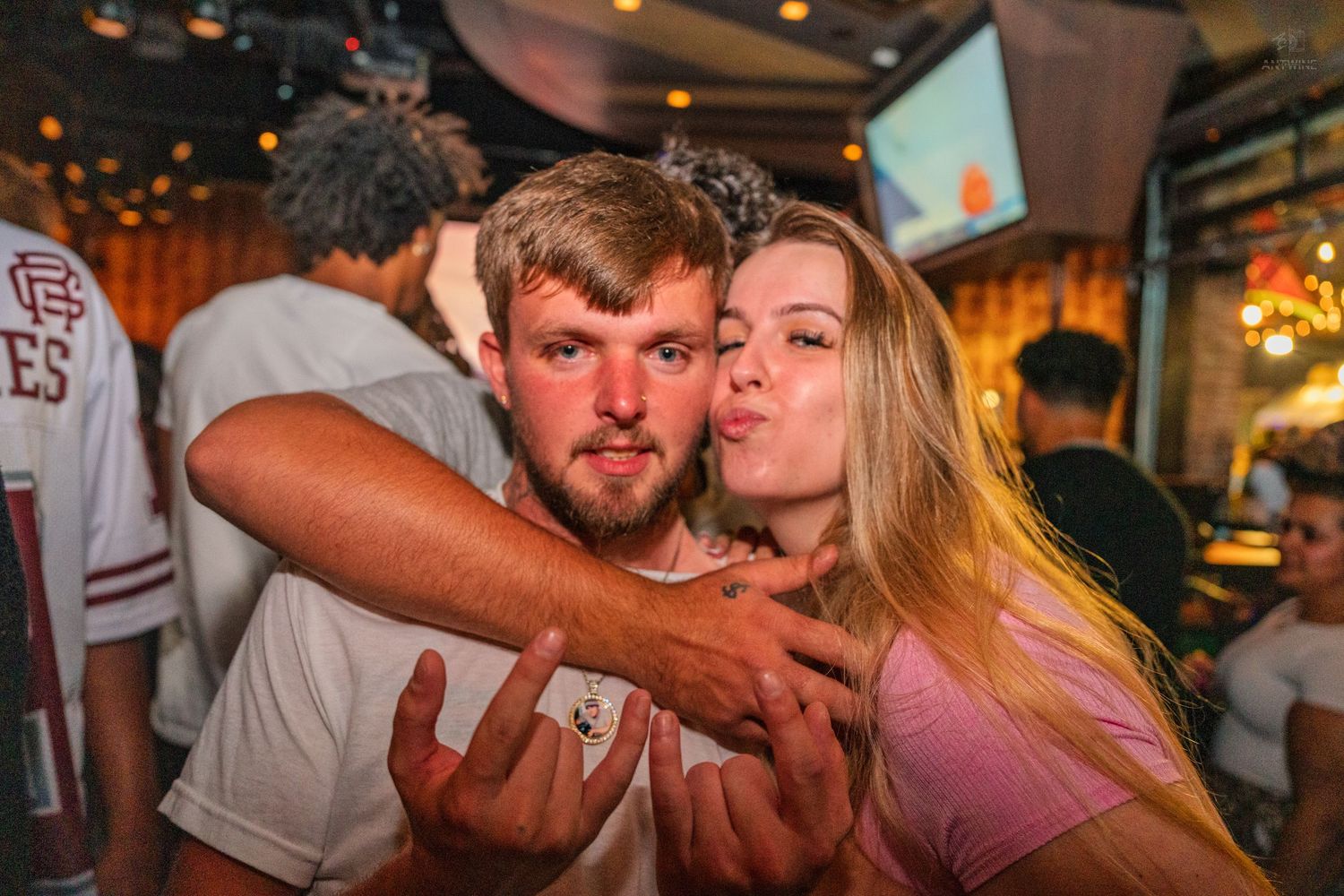 Young couple posing together at a bar, woman making a kissing face behind the man.