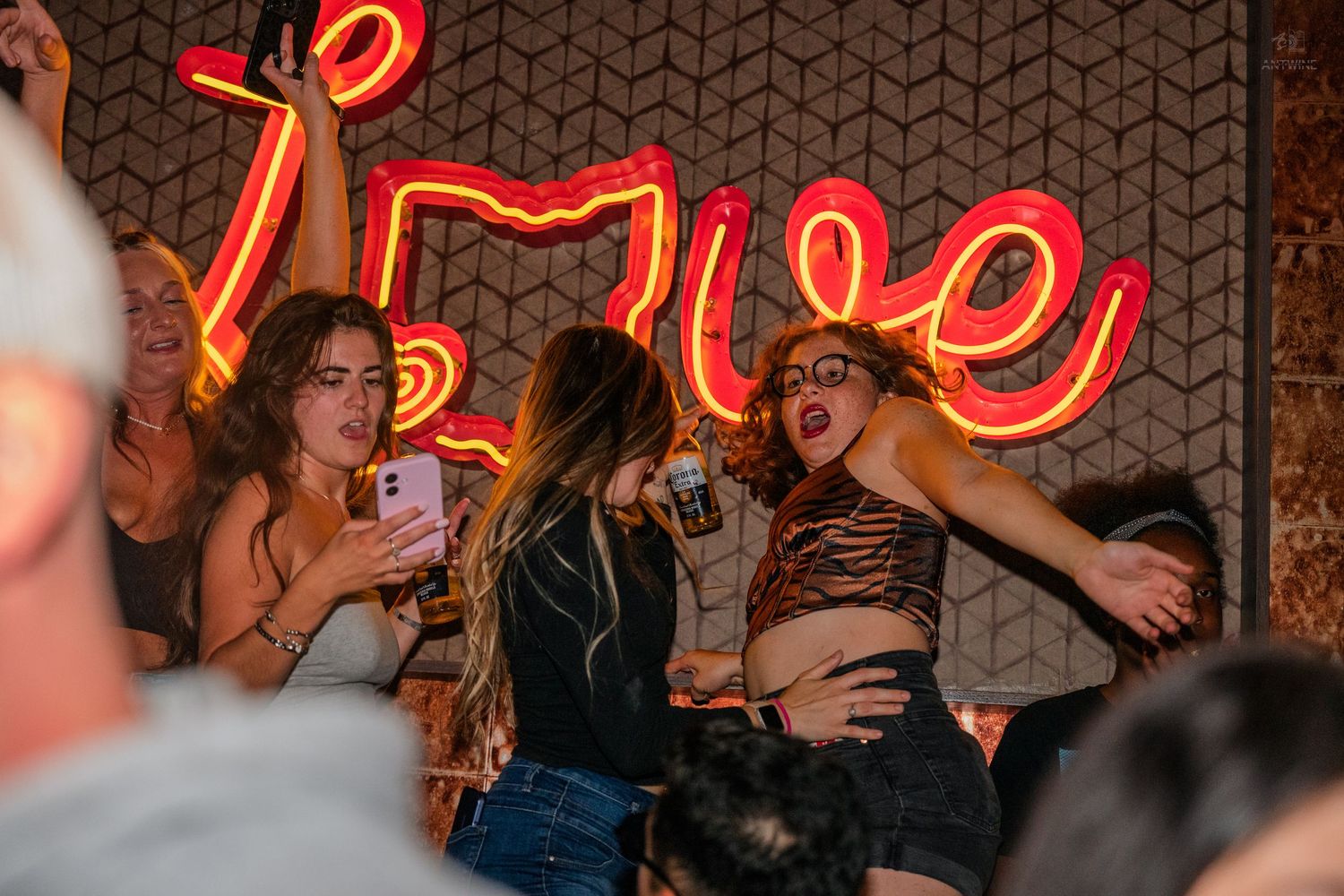 Excited women dancing and celebrating at a vibrant nightclub with neon lighting.